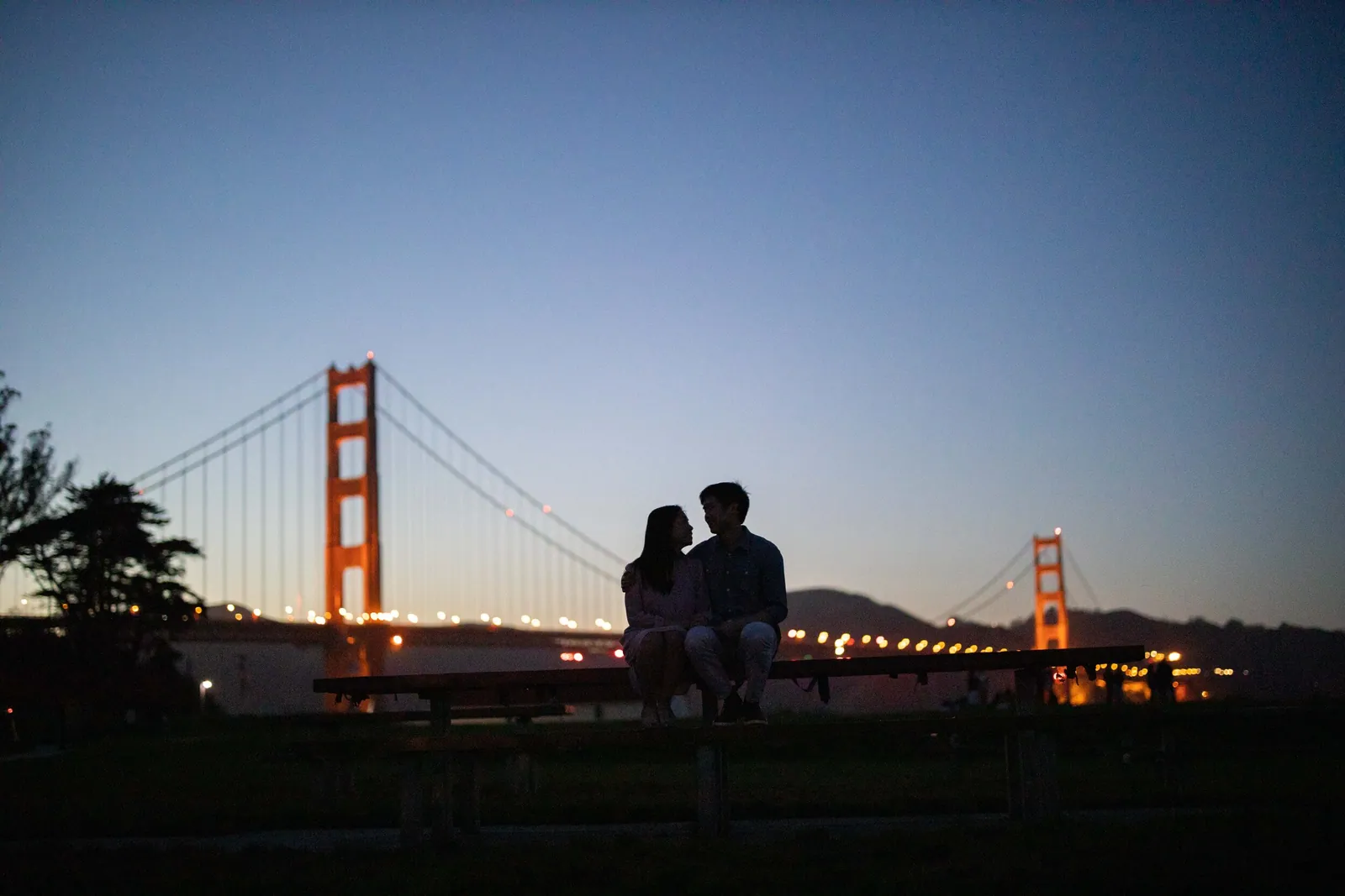 Silhouette of a couple at dusk with the Golden Gate Bridge lit up behind them