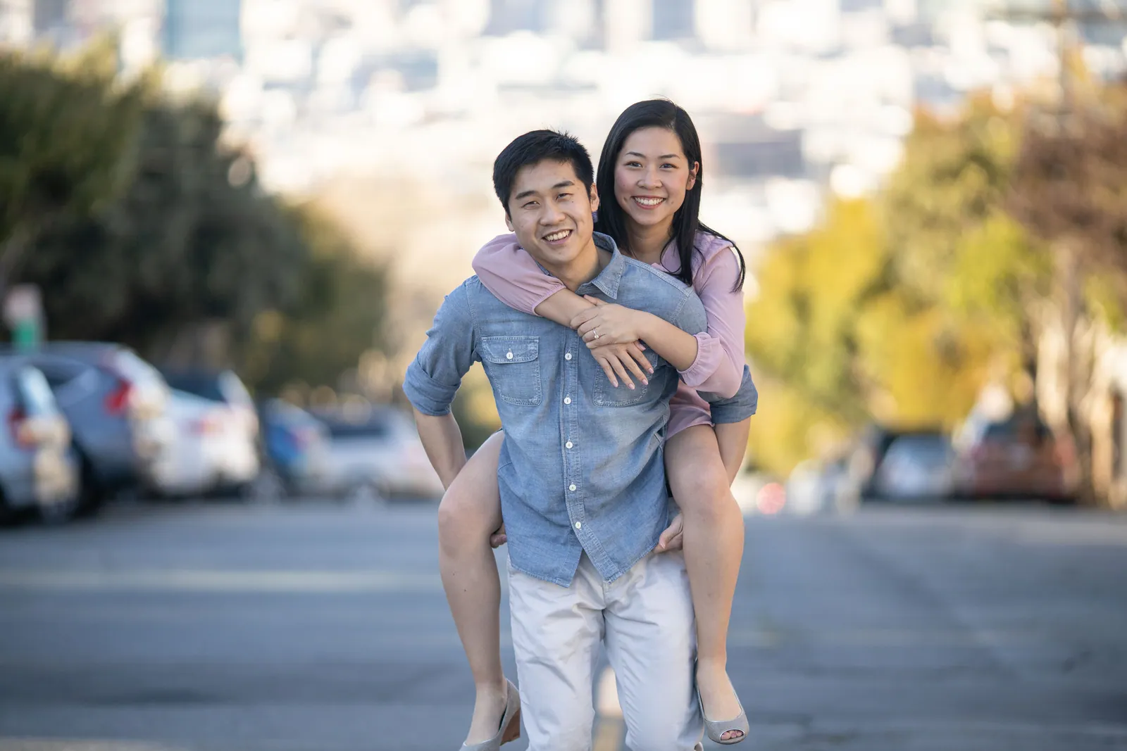 Man carrying his partner piggyback down a city street, both laughing