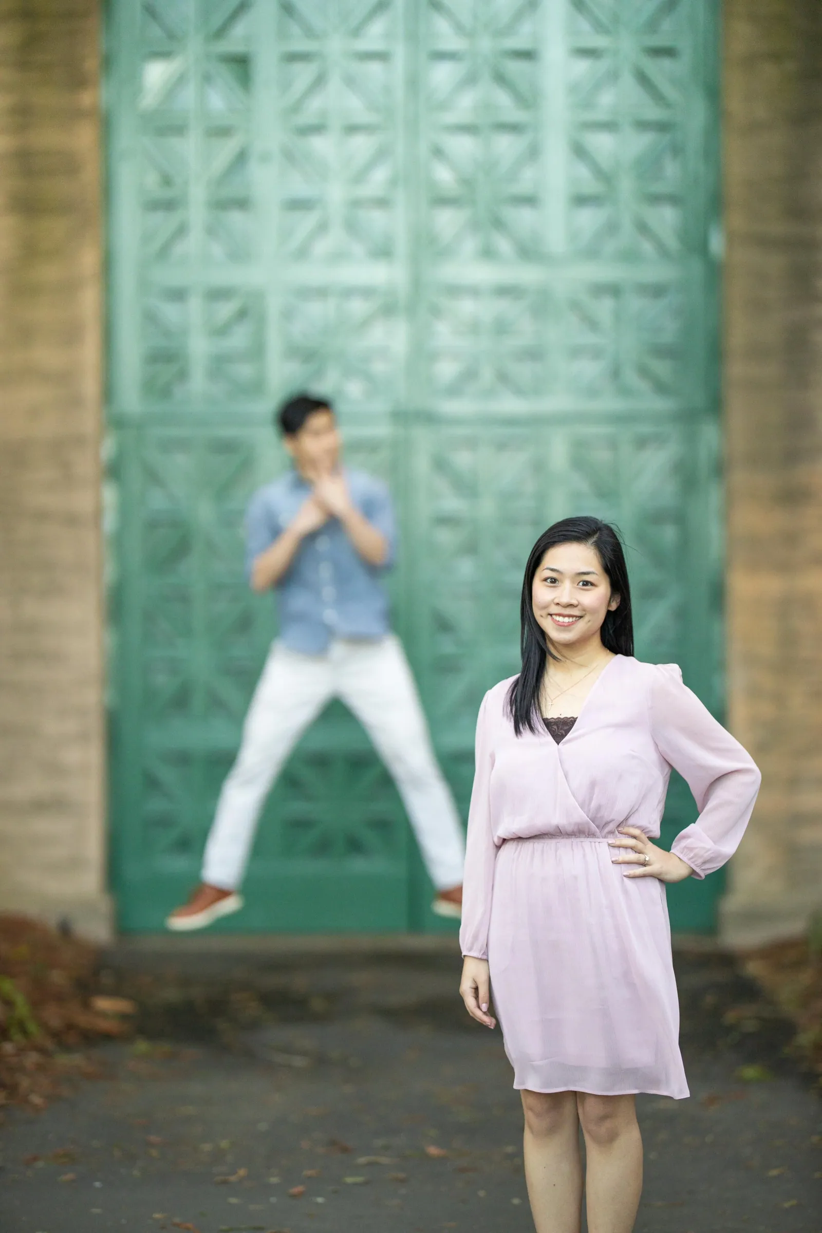 Woman posing in a lilac dress beside a man mid-jump in front of a green patterned door