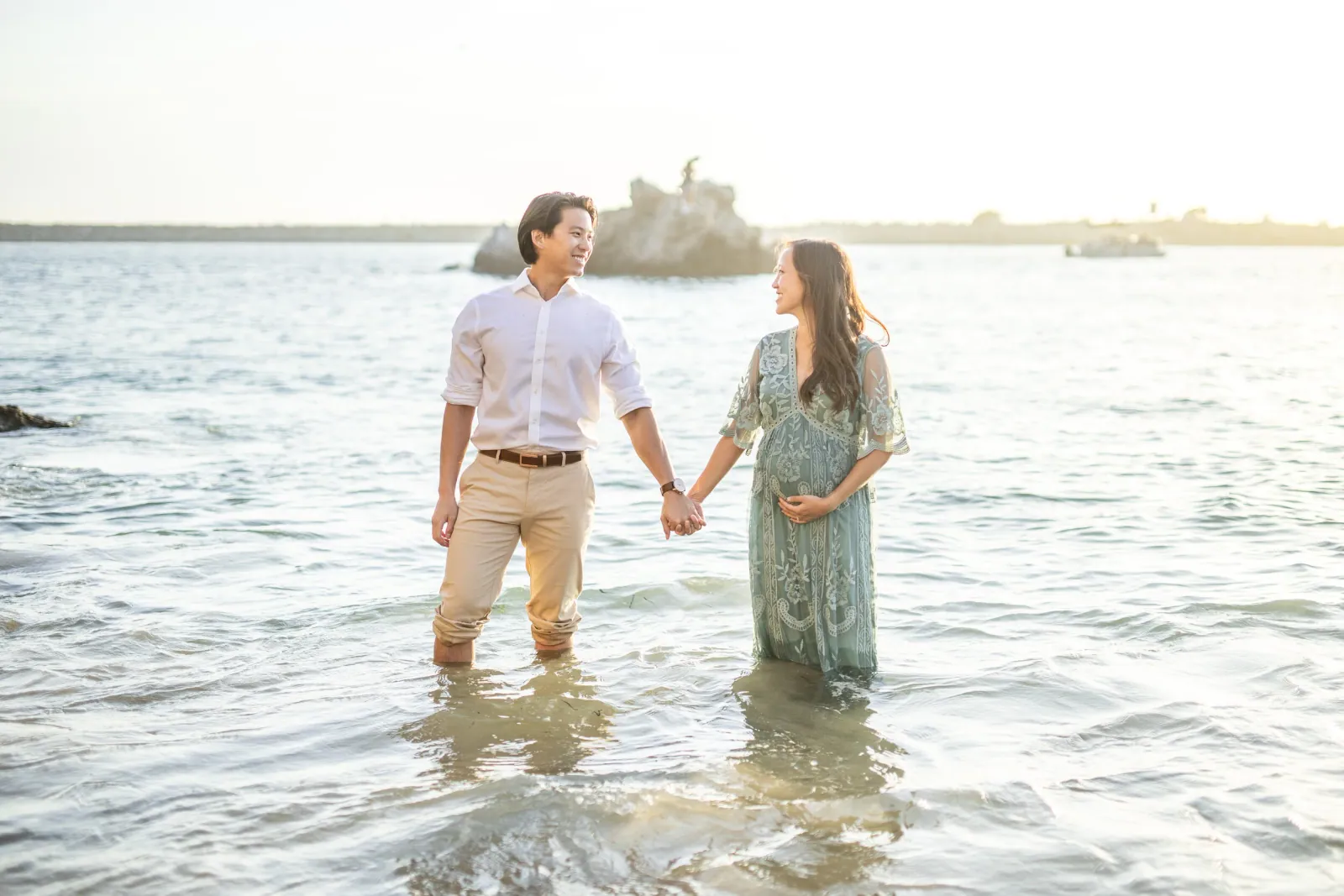 Couple holding hands as they wade in shallow water at sunset