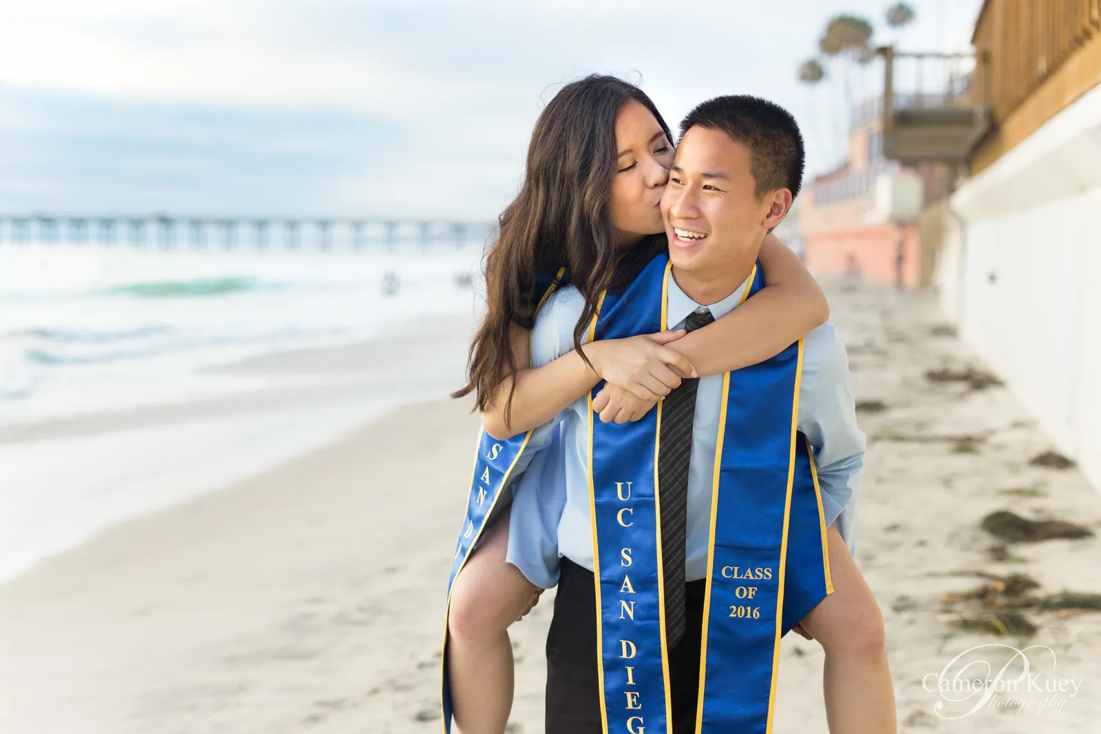 Graduate in a blue stole being carried piggyback along the beach