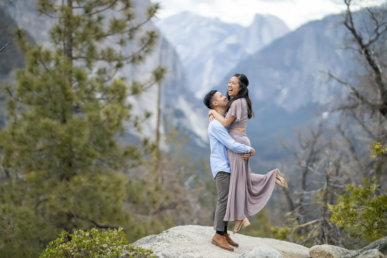 Couple embracing on a granite ledge with Yosemite's Half Dome behind