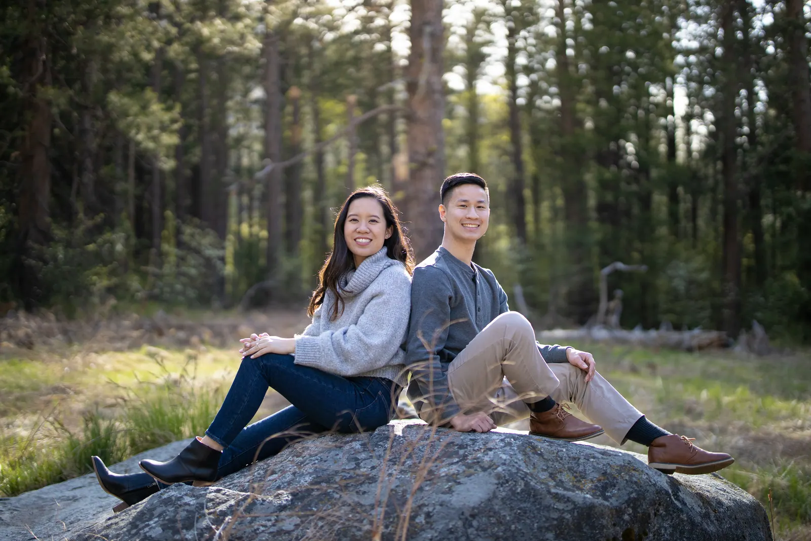 Couple sitting on a large boulder in a pine forest meadow