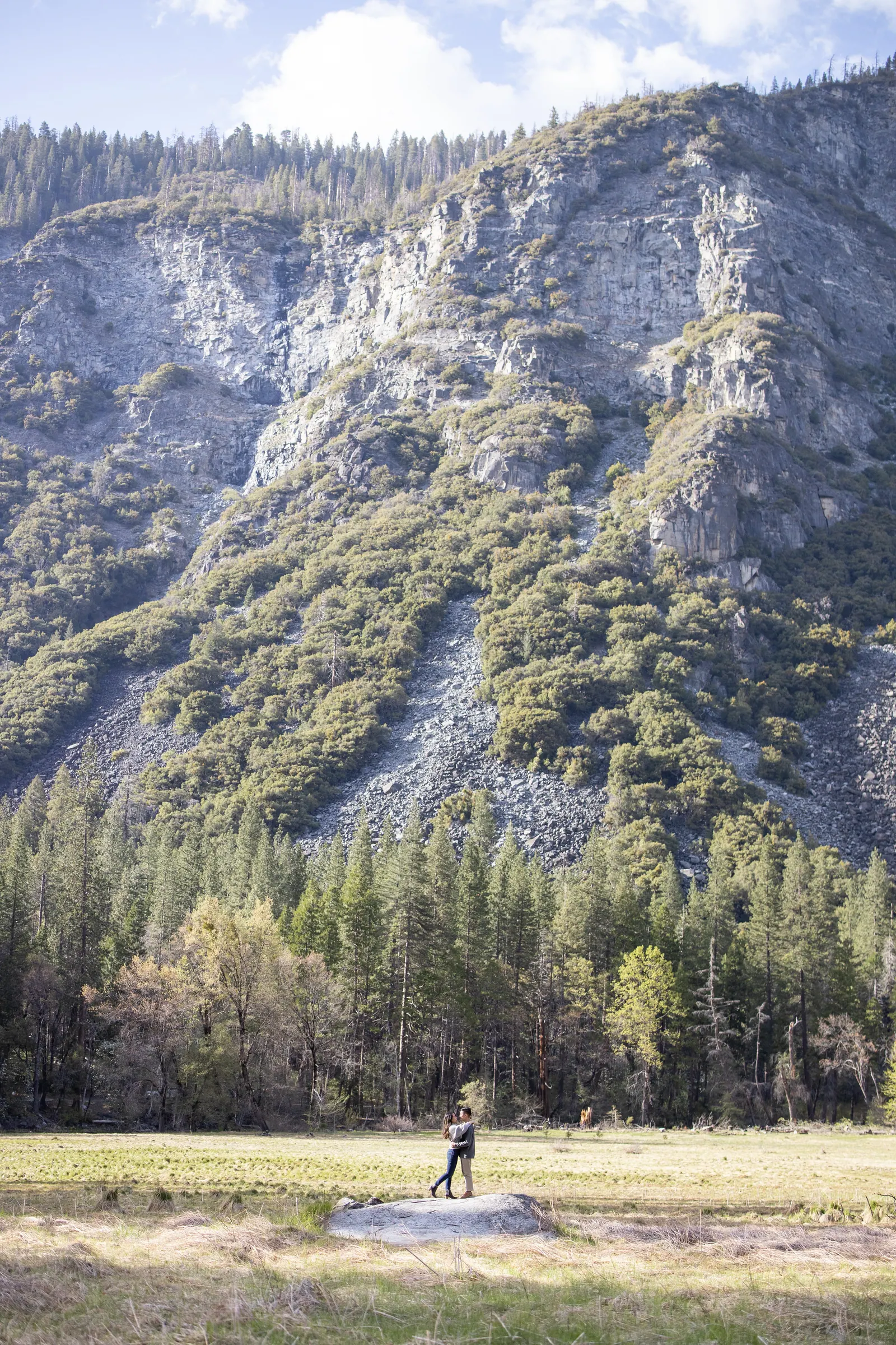 Tiny couple in a meadow below a towering granite cliff
