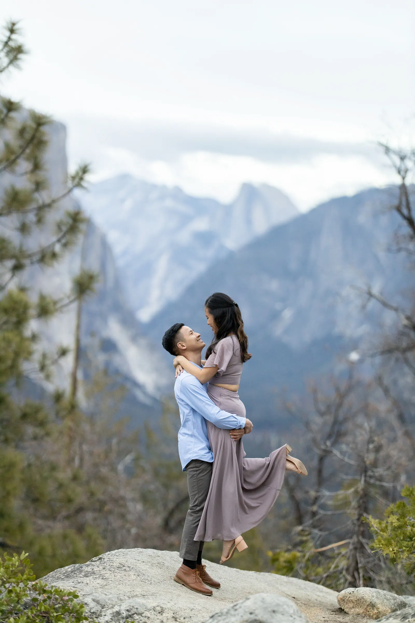 Couple embracing on a granite outcrop with Yosemite Valley behind them