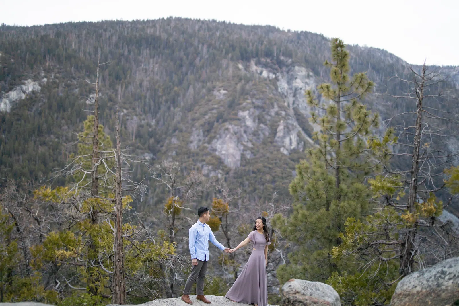 Couple on a rocky overlook with forested mountains behind