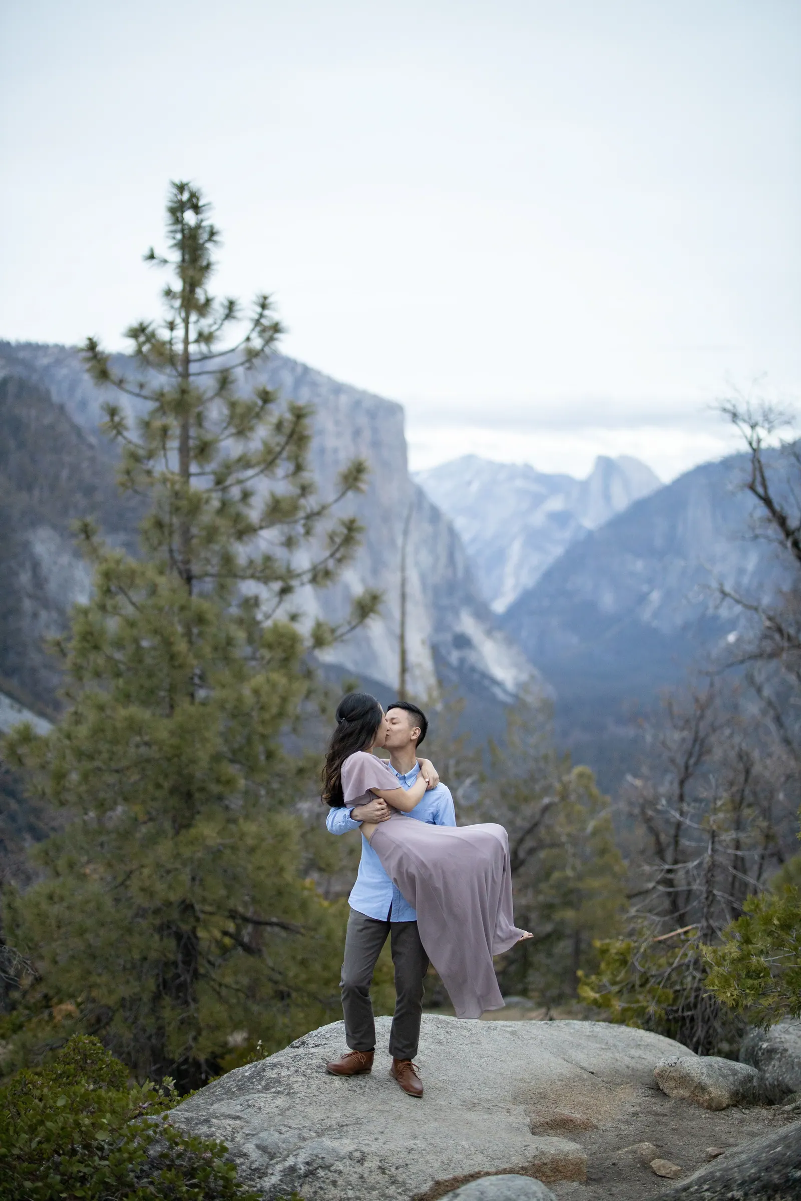 Man lifting his fiancée on a granite point above the valley