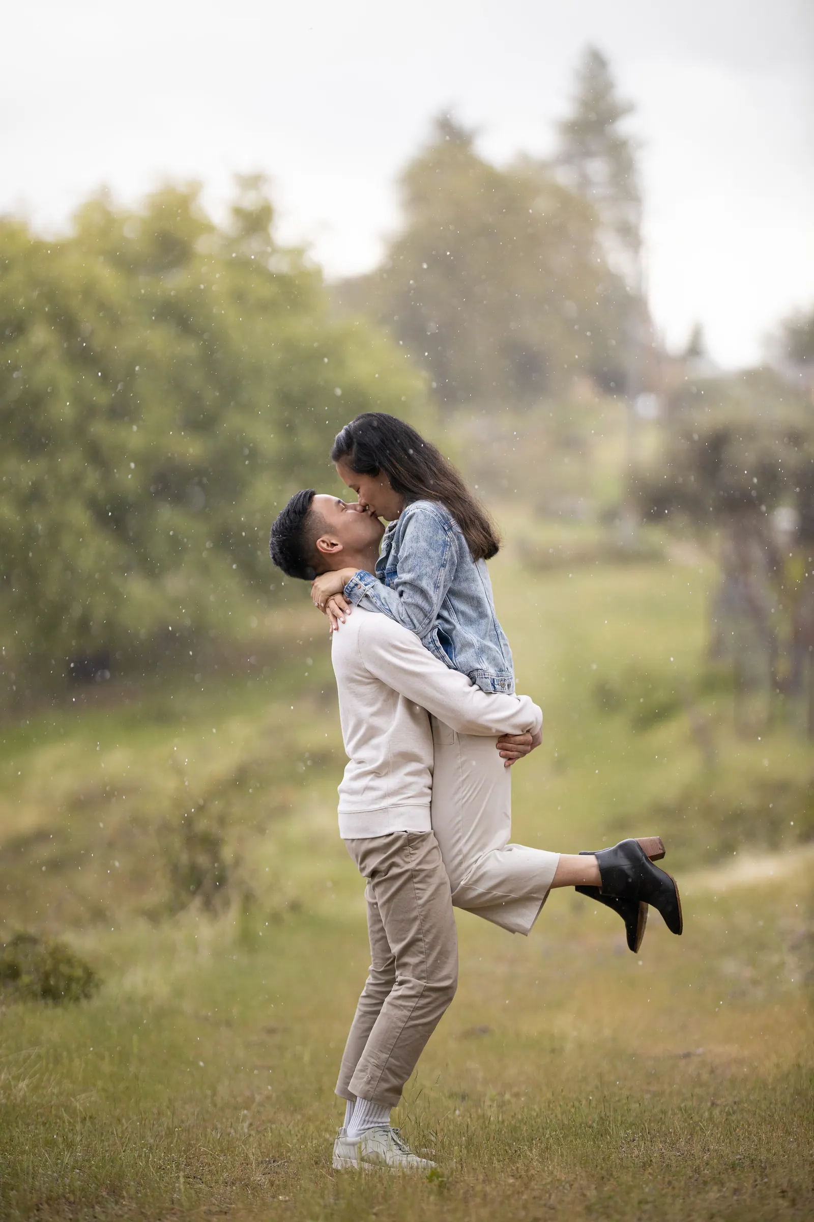 Man lifting his fiancée in a grassy meadow