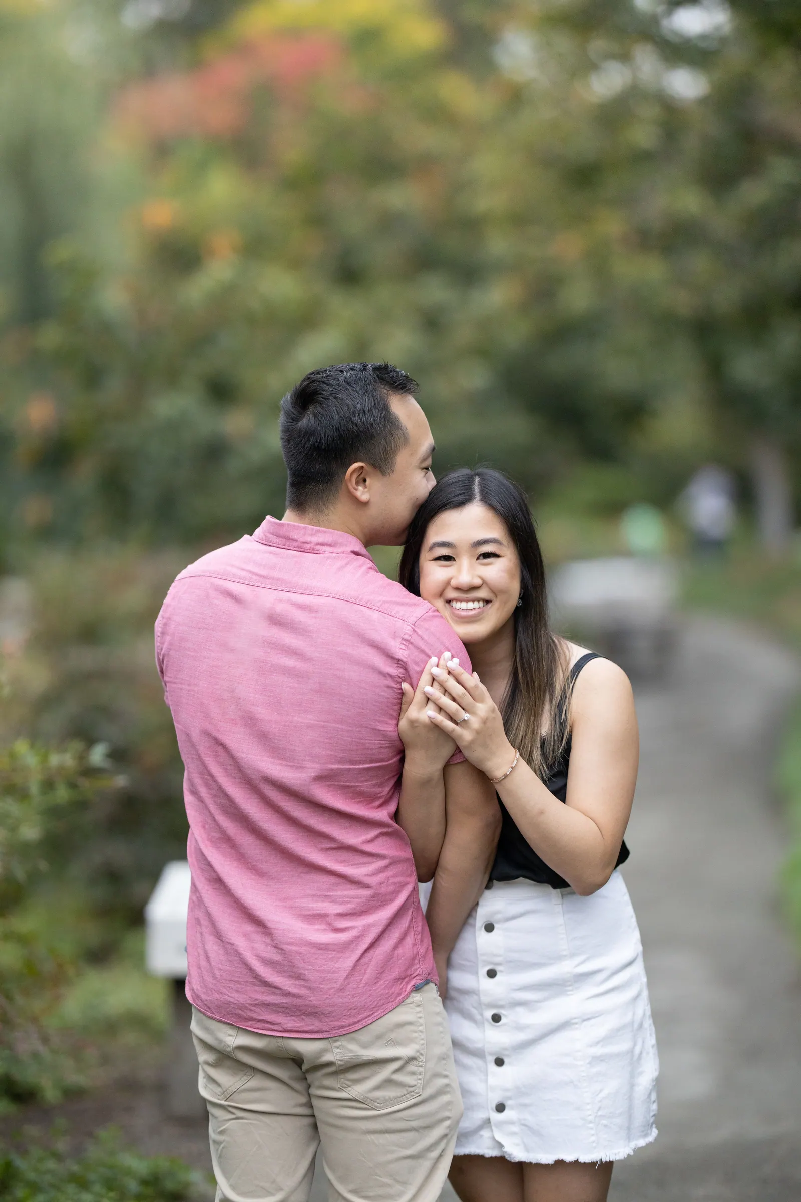 Man kissing his fiancée's forehead among autumn trees