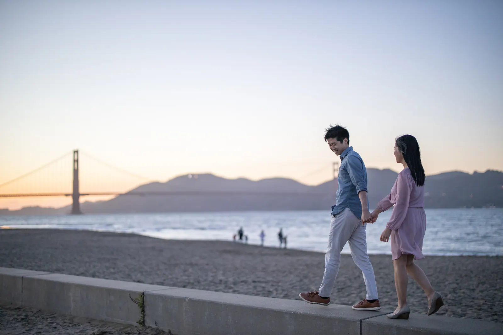 Couple walking on the beach at dusk with the Golden Gate Bridge behind