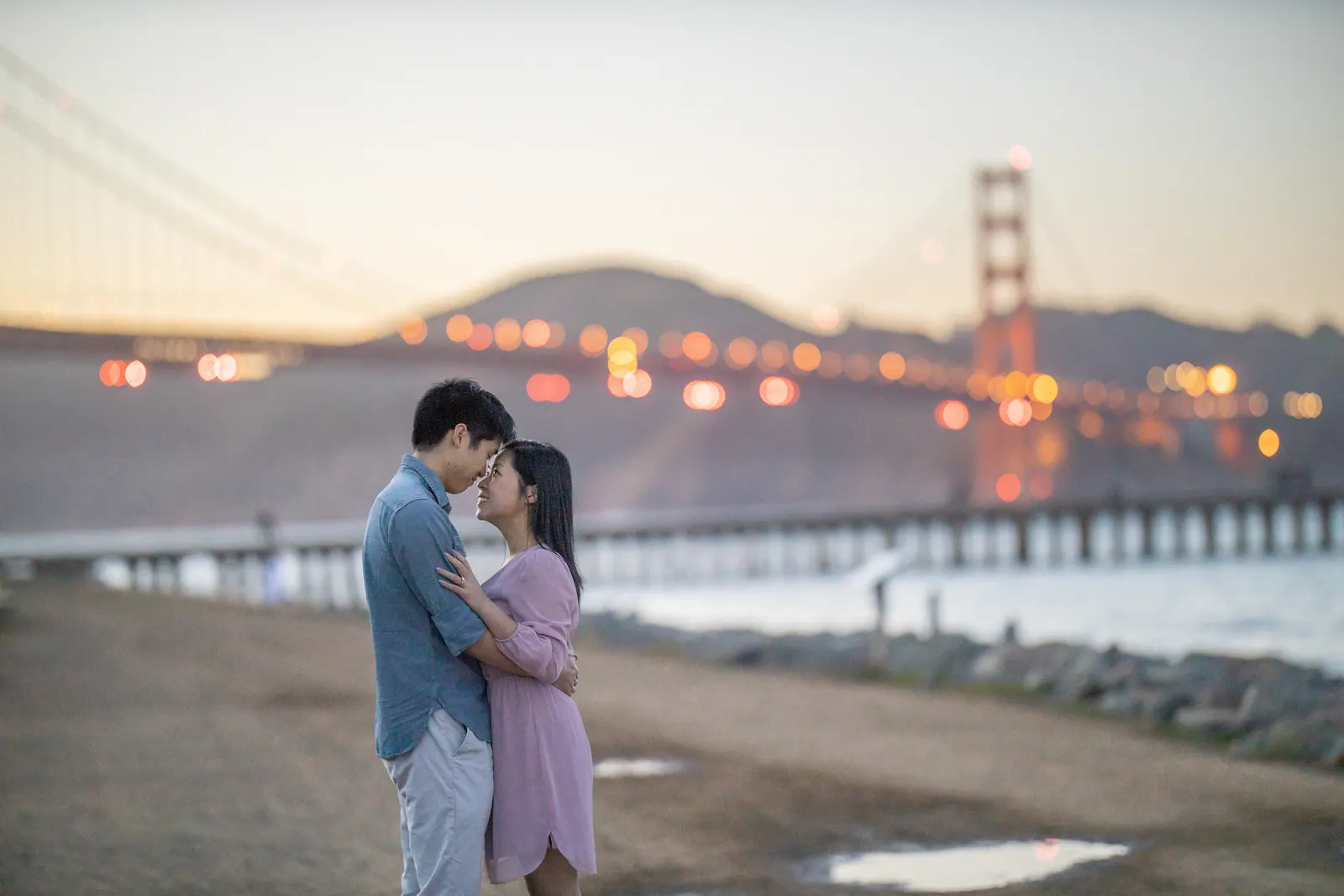 Couple embracing at sunset with the Golden Gate Bridge in the distance