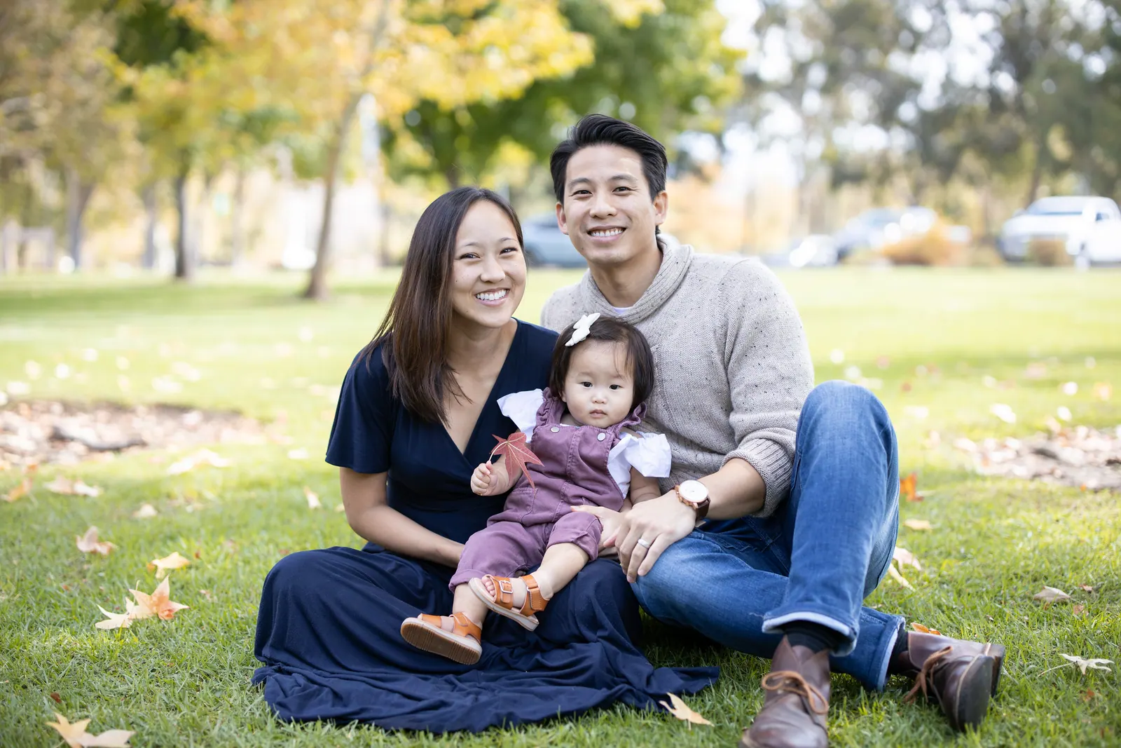Parents sitting on the grass with their toddler daughter in a park