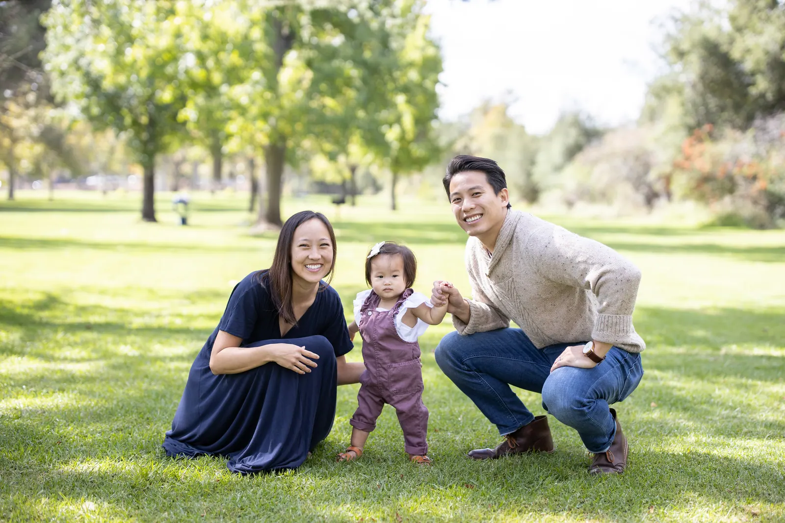 Parents crouching with their toddler on a park lawn
