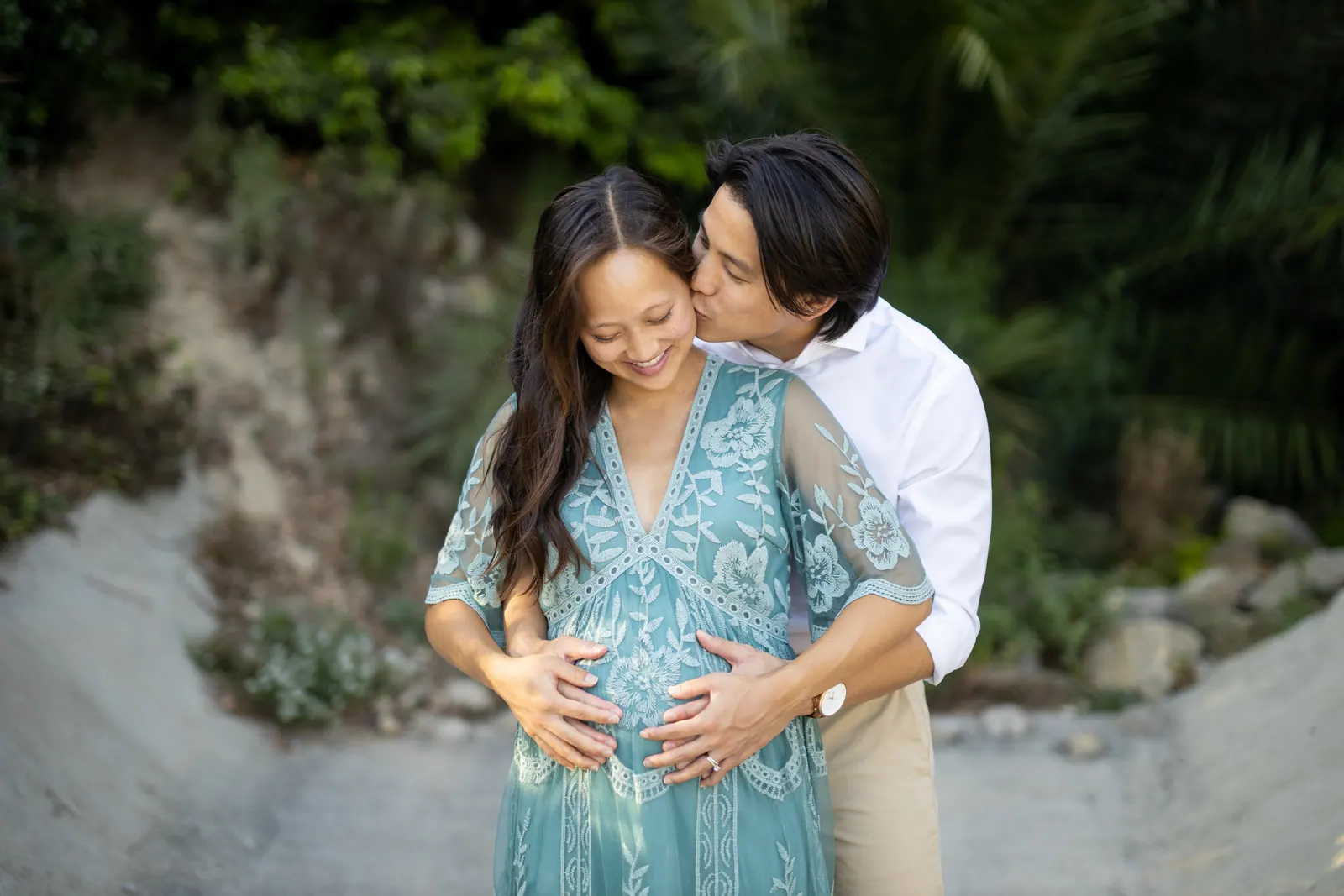 Maternity portrait: man kissing his pregnant wife among greenery
