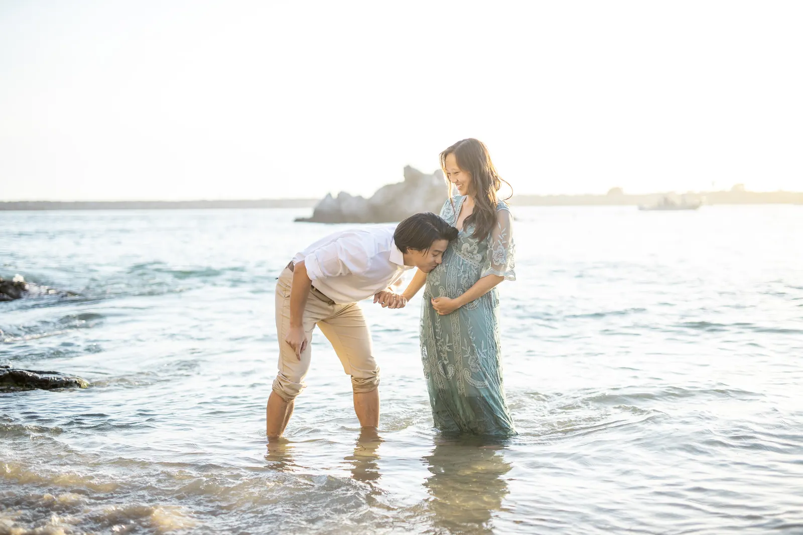 Man kissing his pregnant wife's belly in the shallow surf