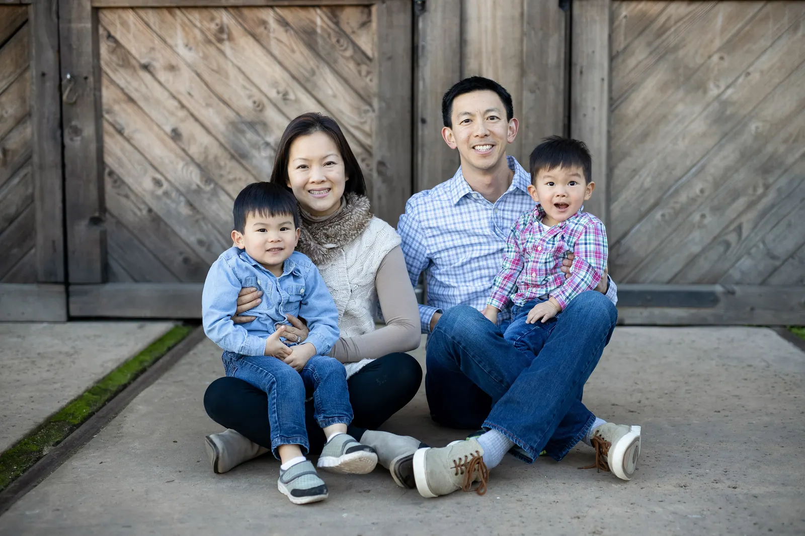 Family with two young boys sitting in front of a wooden barn door