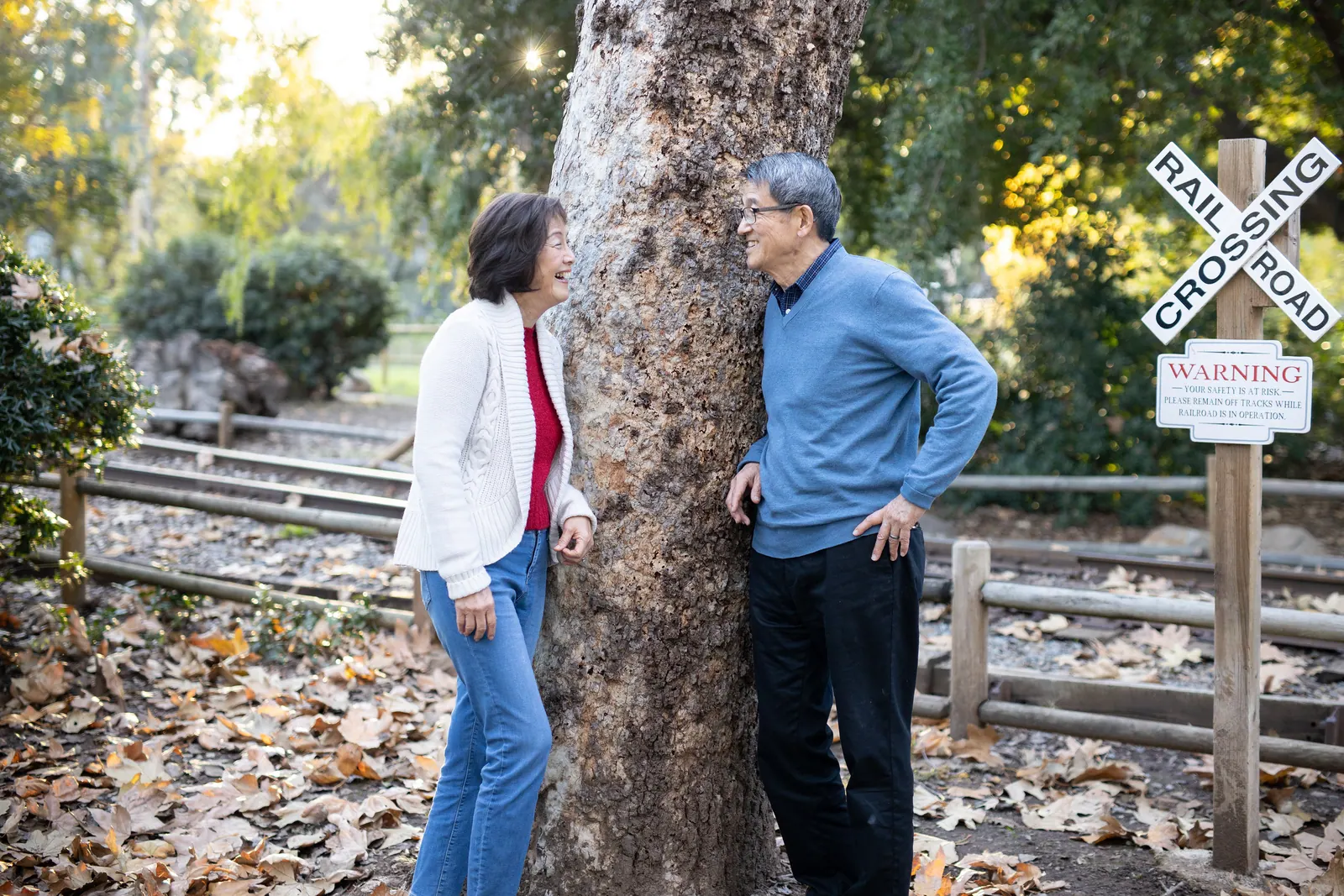 Couple standing by a tree next to a railroad crossing sign