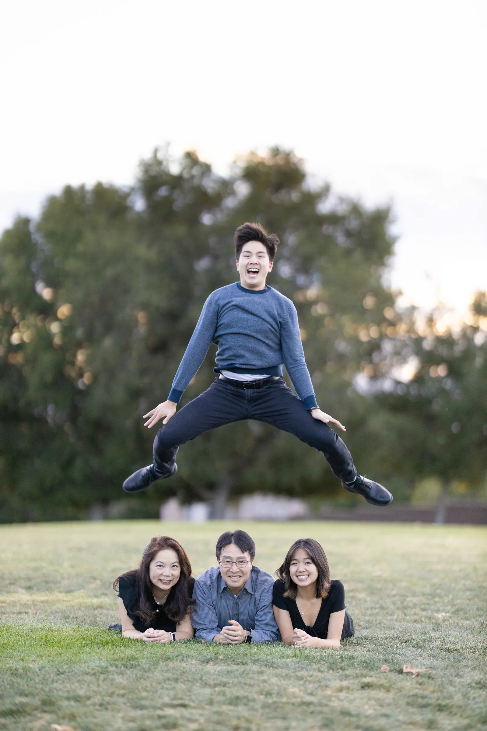 Man jumping mid-air above family members lying on the grass