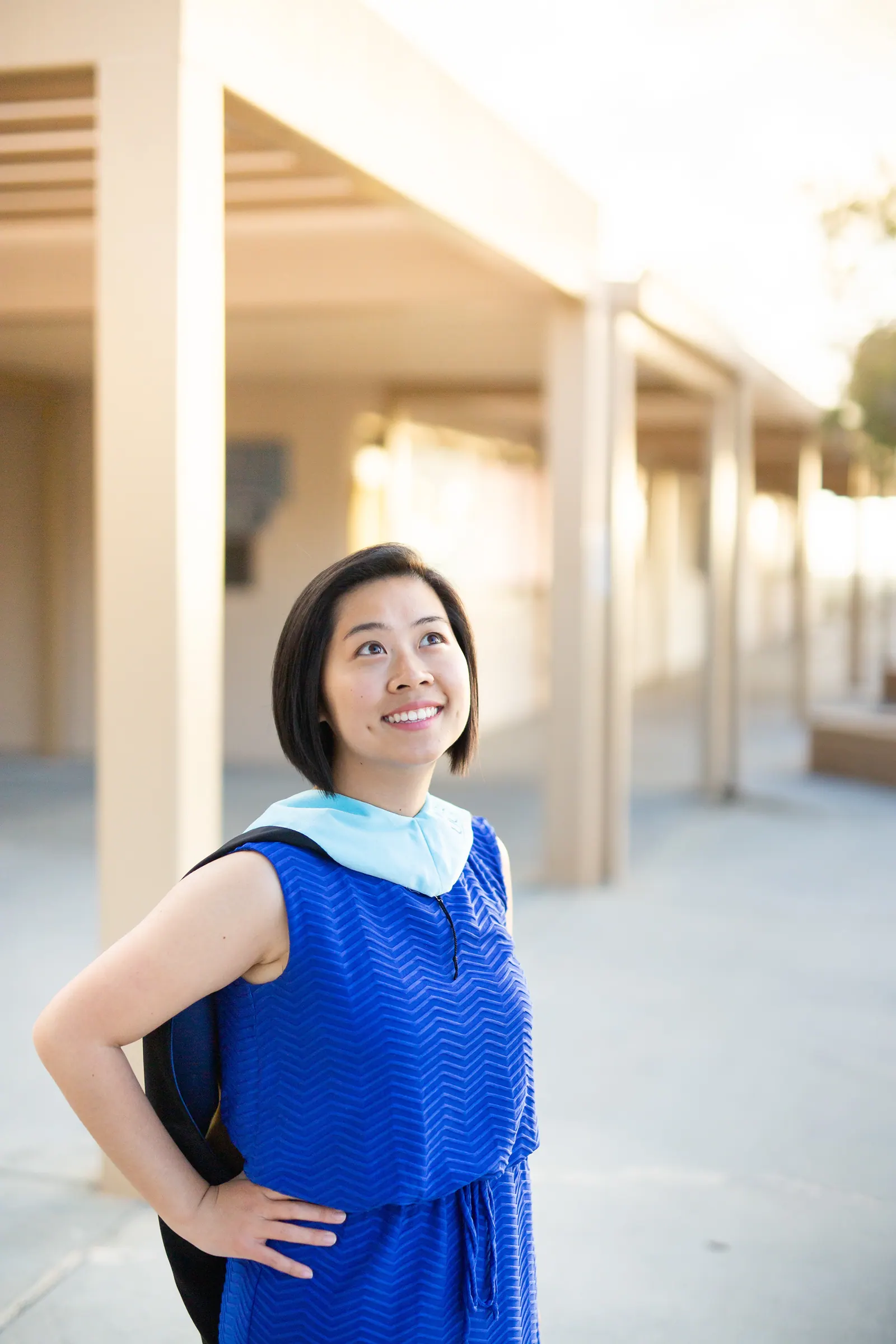 Graduate in a blue dress and stole in a sunlit corridor