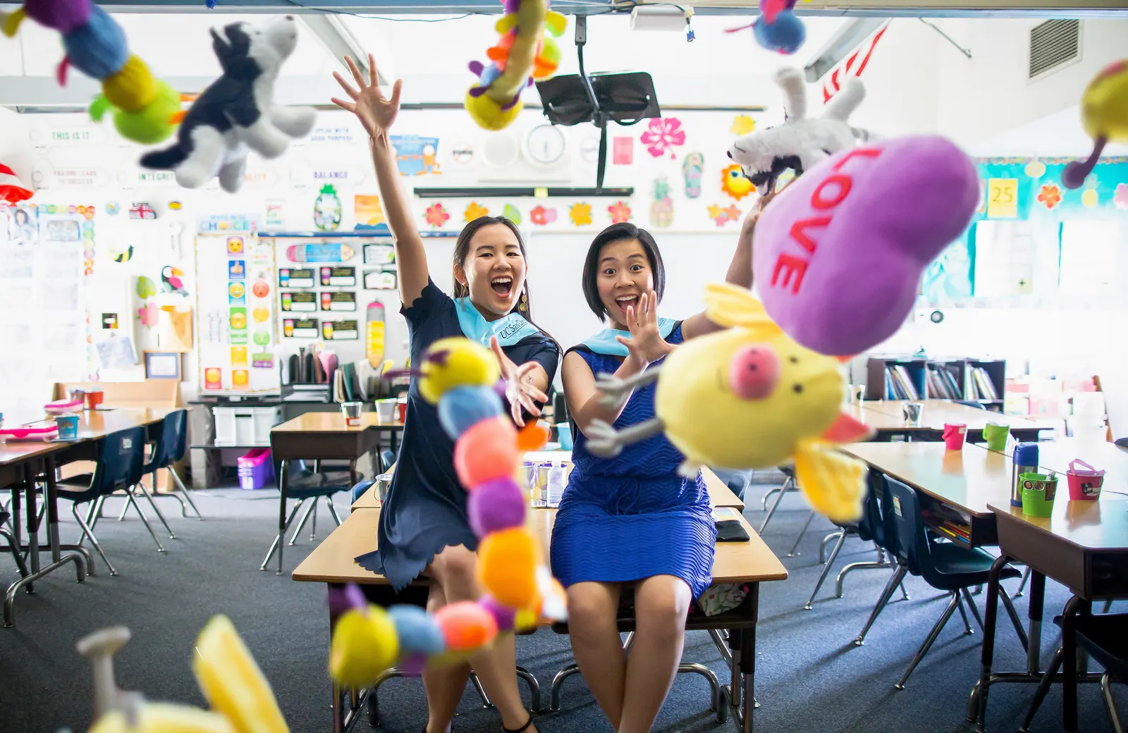 Two teachers celebrating graduation in a colorful classroom with balloons