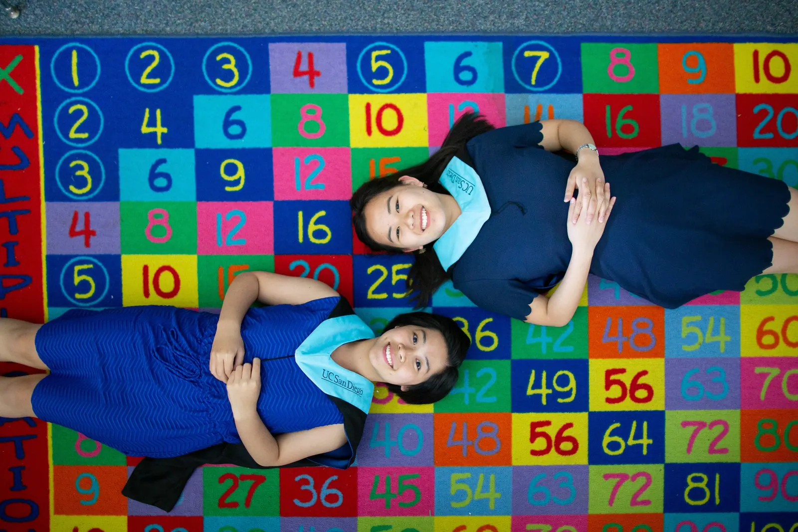Two graduates lying on a numbered classroom rug