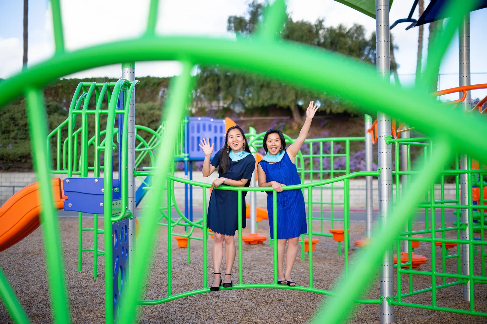 Two graduates posing on a green playground climbing structure