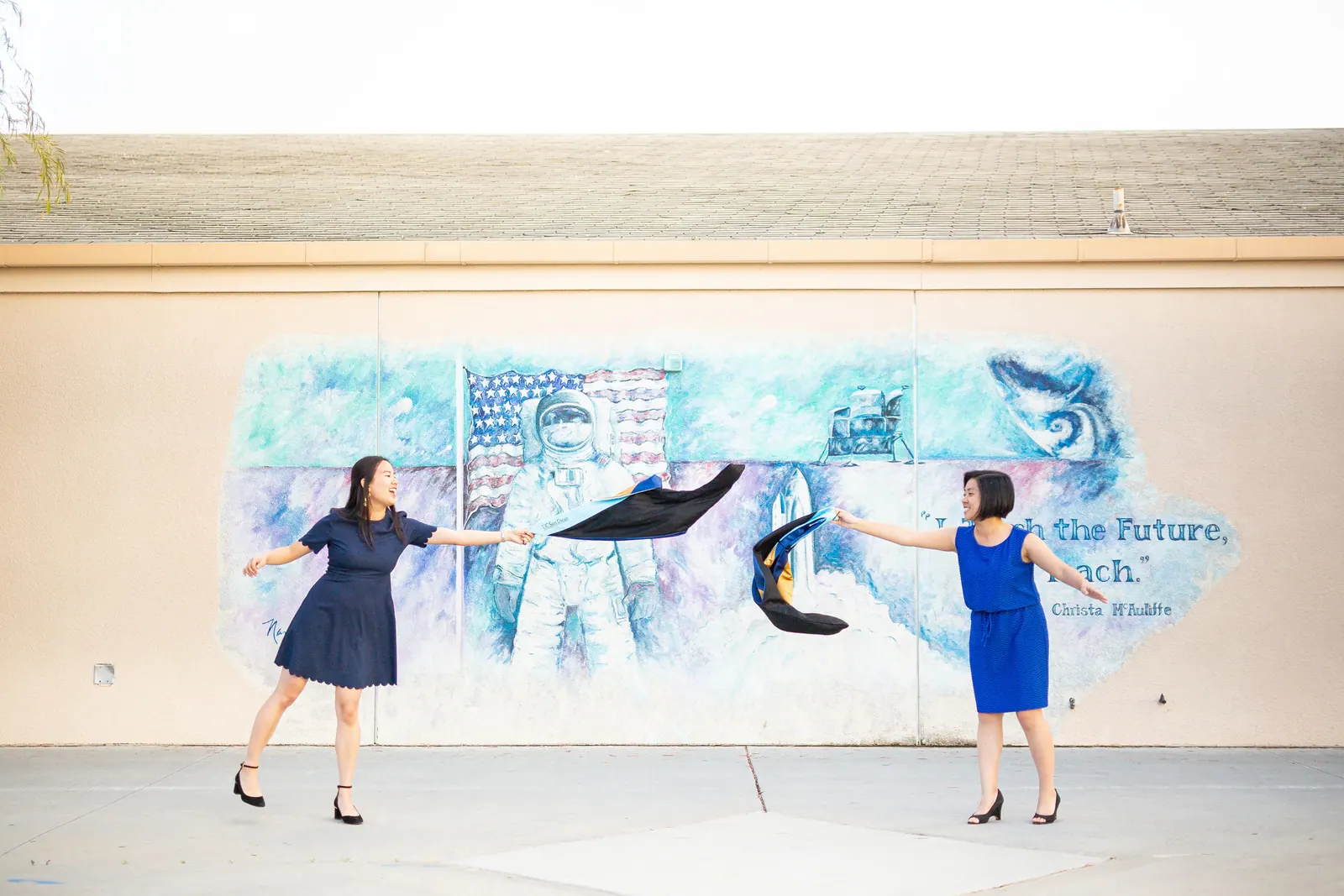 Two graduates jumping in front of a painted mural