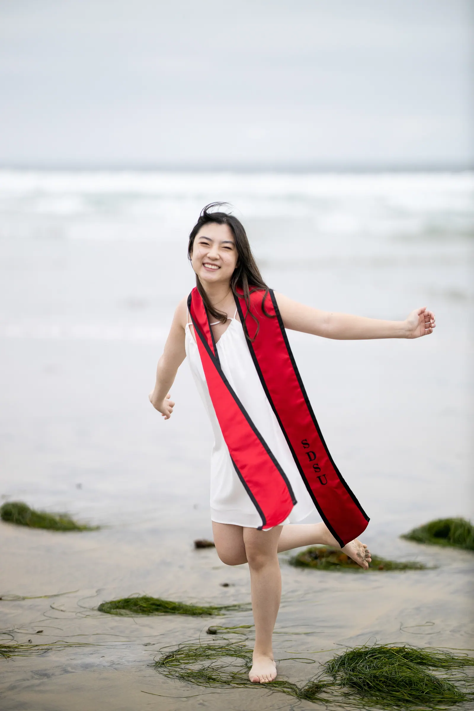 Graduate in a red stole kicking up her heel on the beach