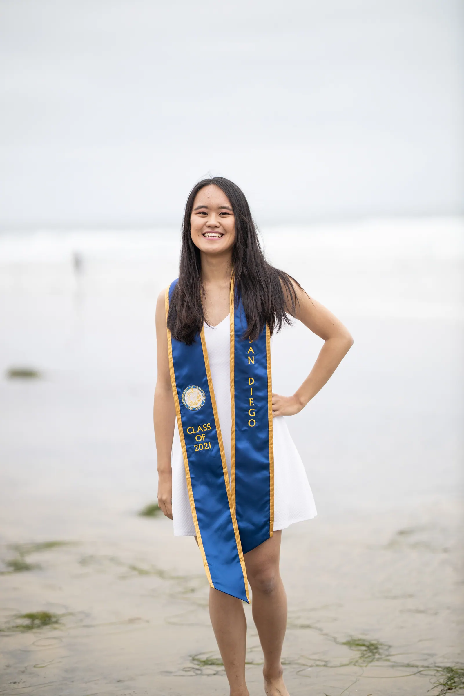 Graduate in a white dress and blue stole on the beach