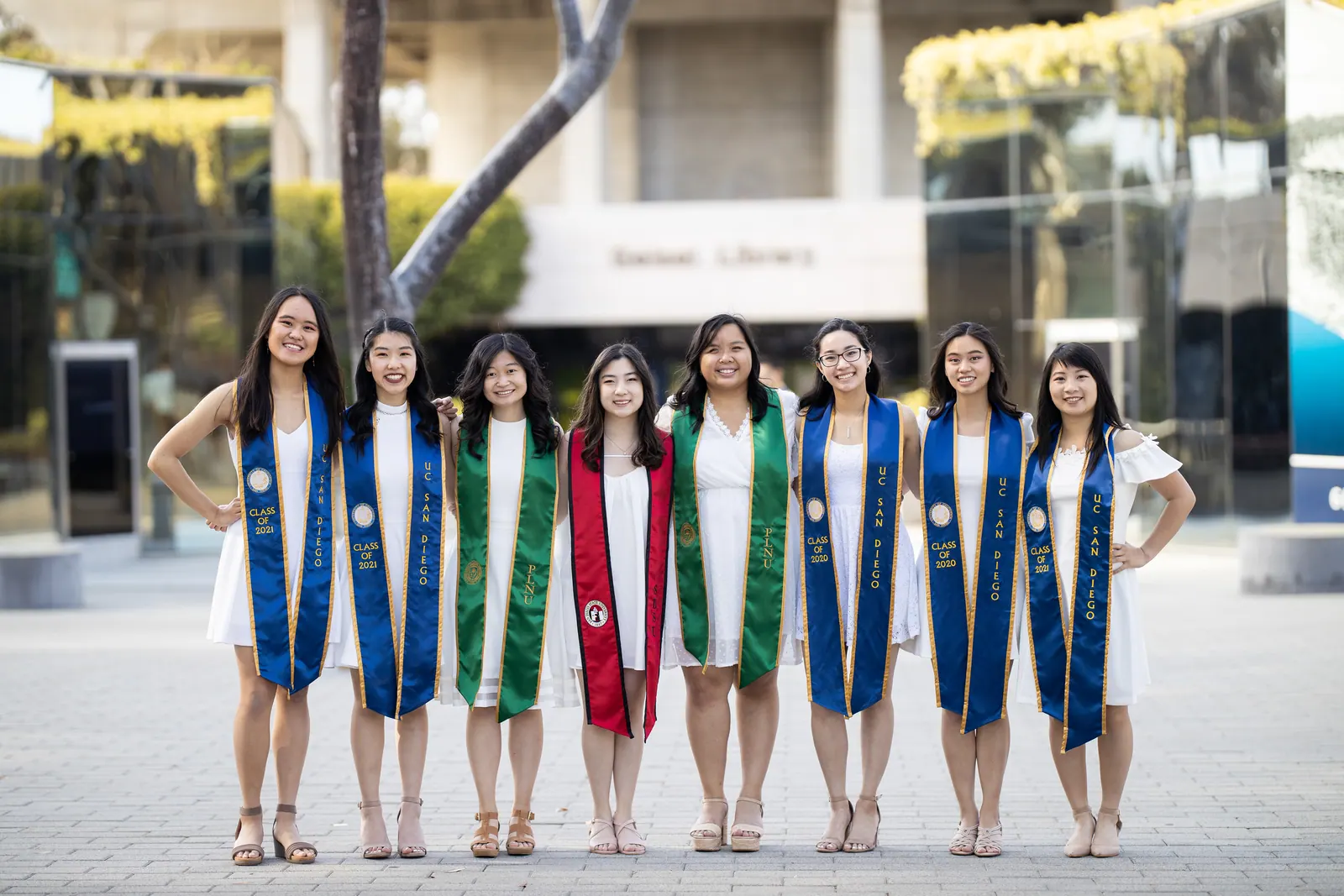 Group of graduates with stoles in front of a campus building