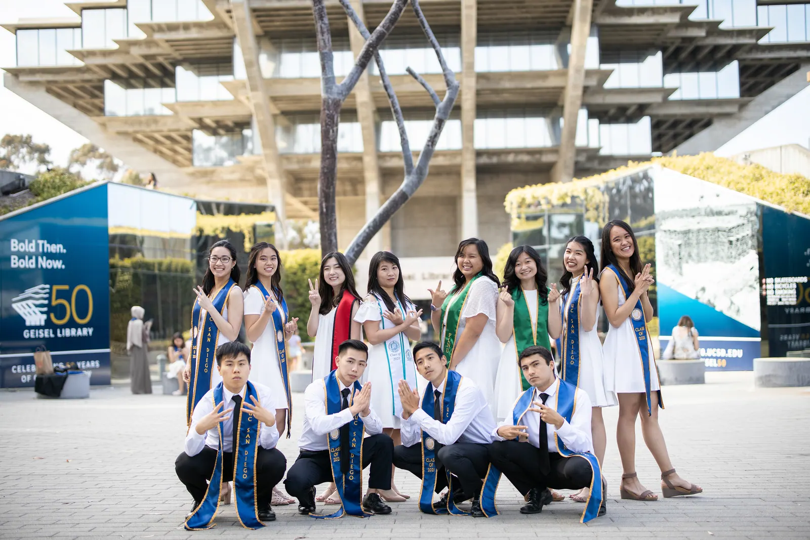 Group of graduates sitting and standing under a campus structure