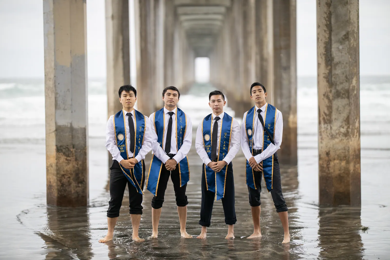 Male graduates in stoles standing under a pier