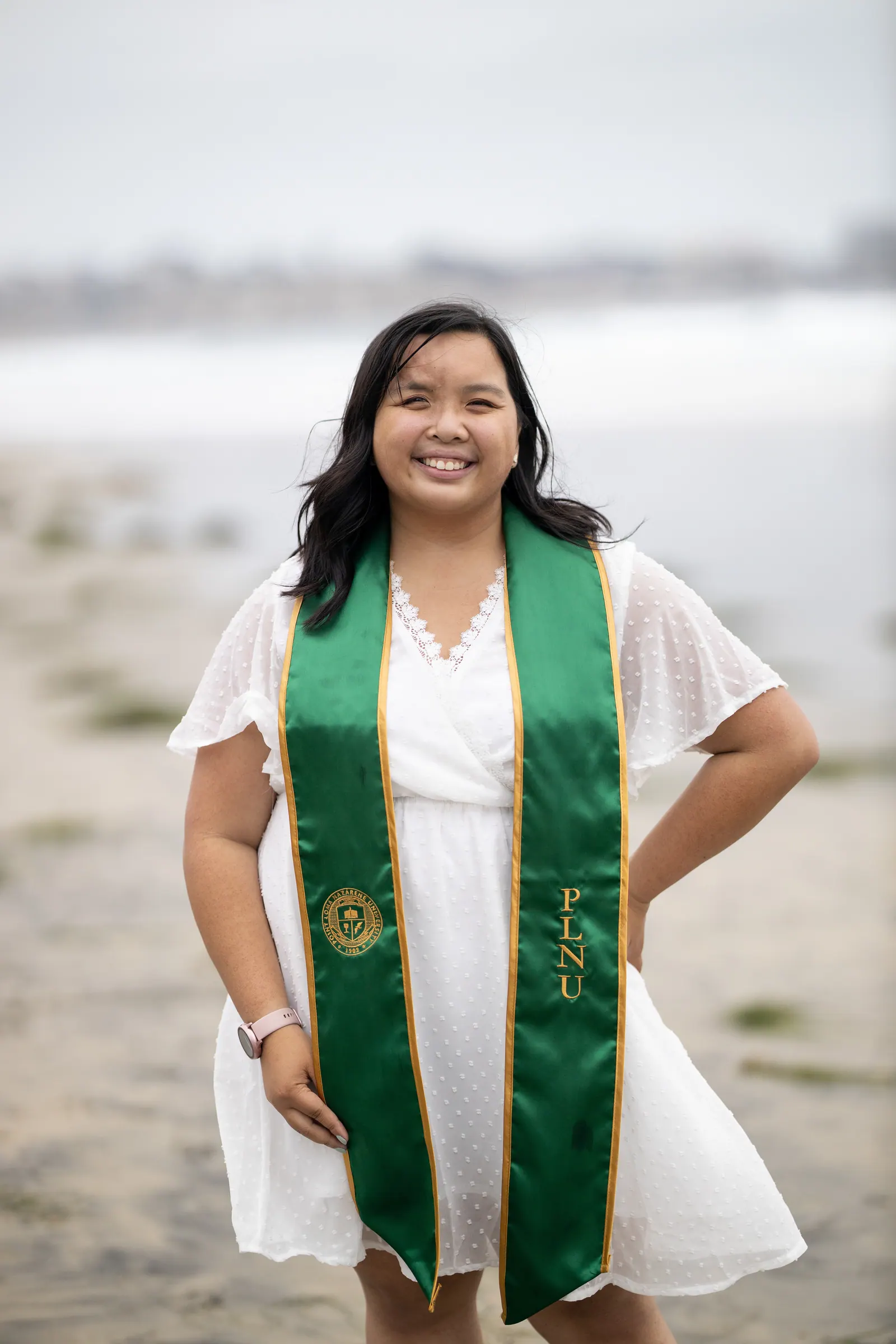 Graduate in a white dress and green stole on the beach