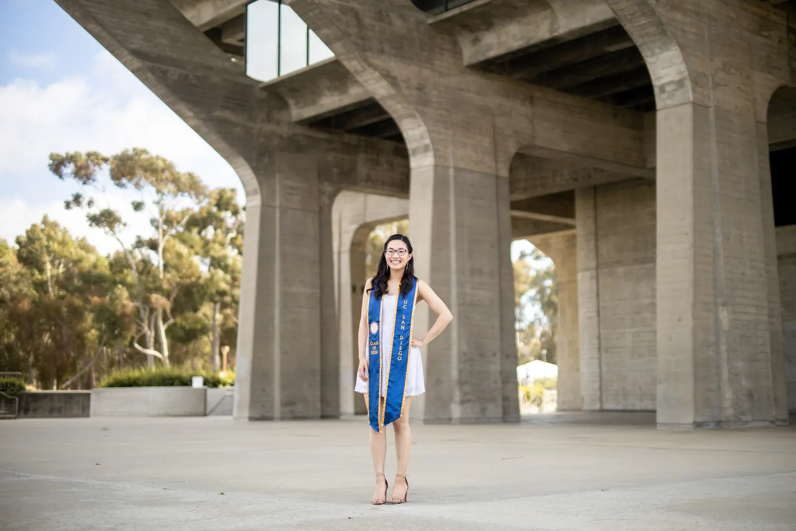 Graduate standing beneath the concrete pillars of a campus building