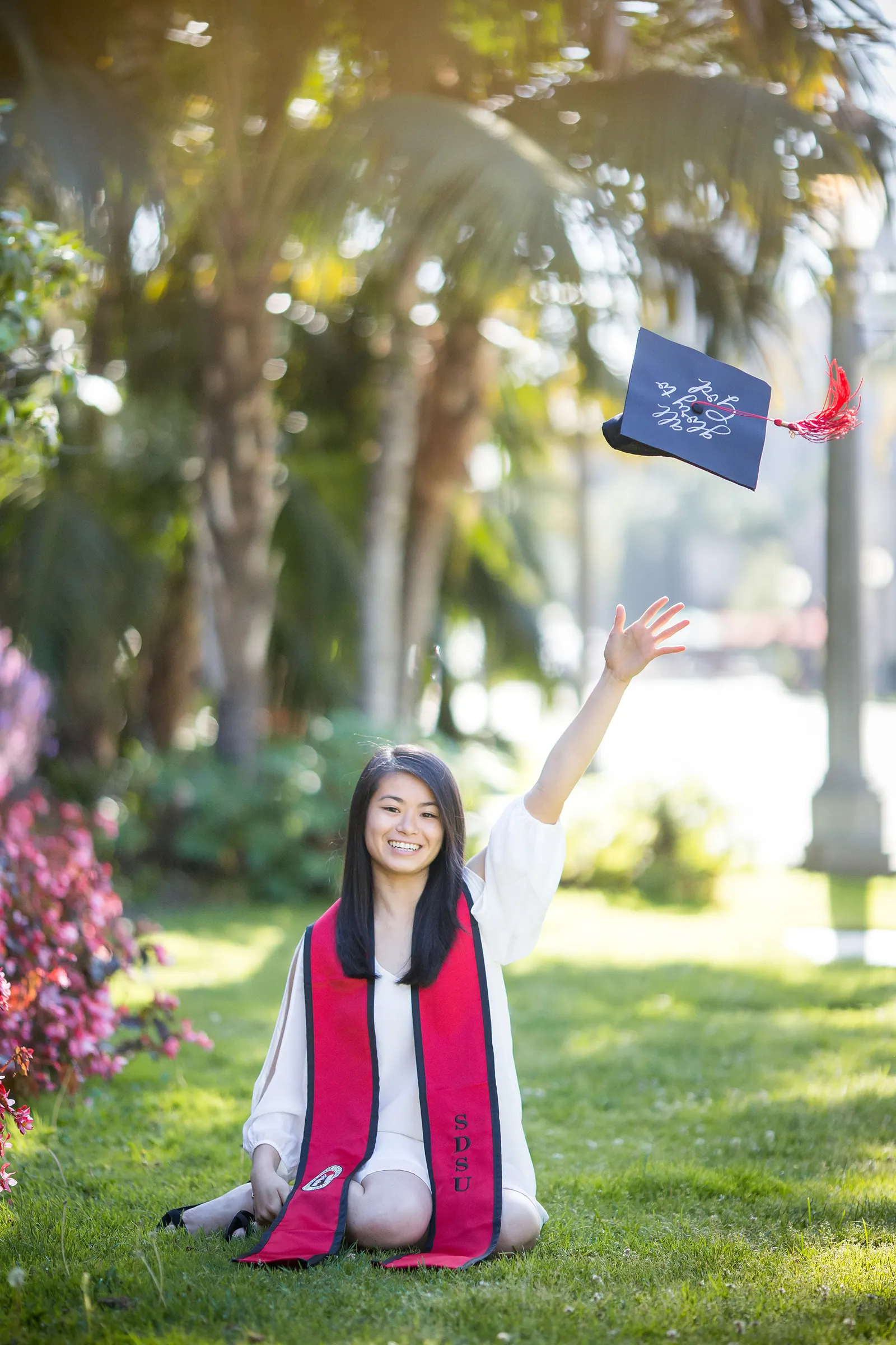 Graduate tossing her cap while sitting on the lawn