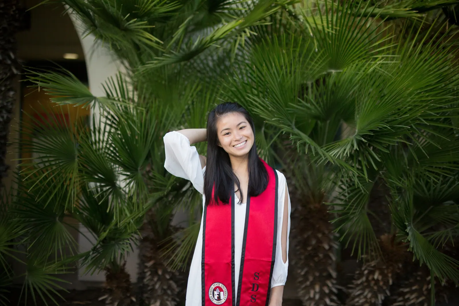Graduate in a red stole among palm fronds