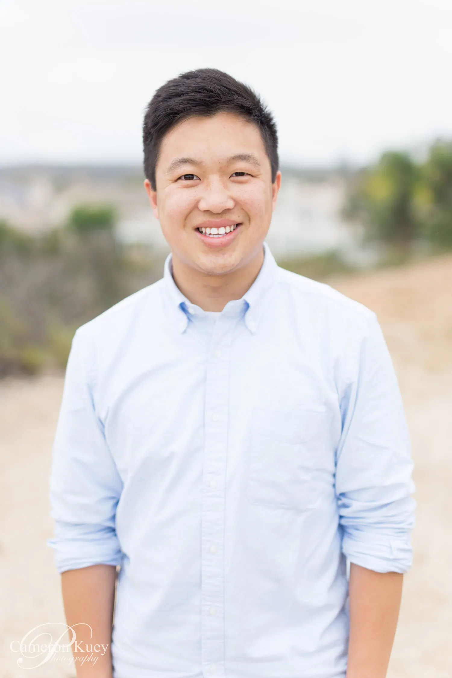 Portrait of Cameron Kuey smiling in a light blue button-down shirt outdoors