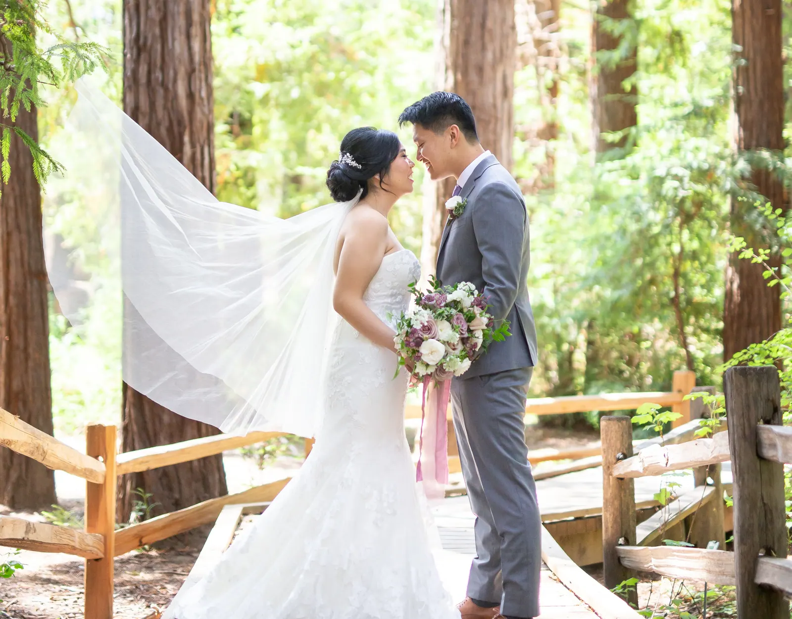 Bride and groom facing each other beside a wooden fence in a redwood forest