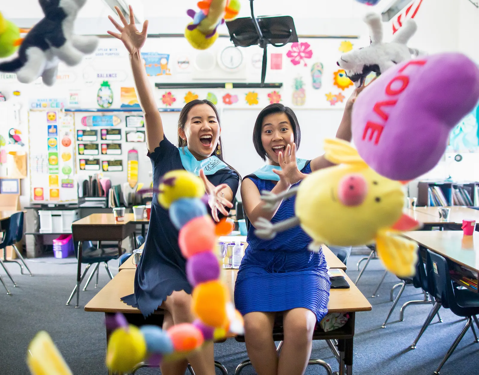 Graduate in a blue dress celebrating in a colorful classroom with balloons
