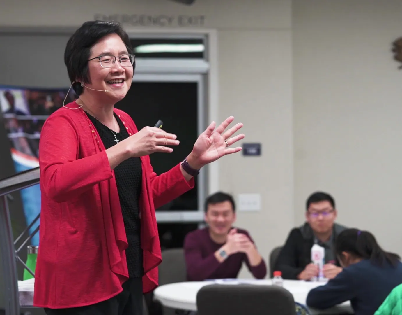 Speaker in a red cardigan gesturing during a filmed workshop