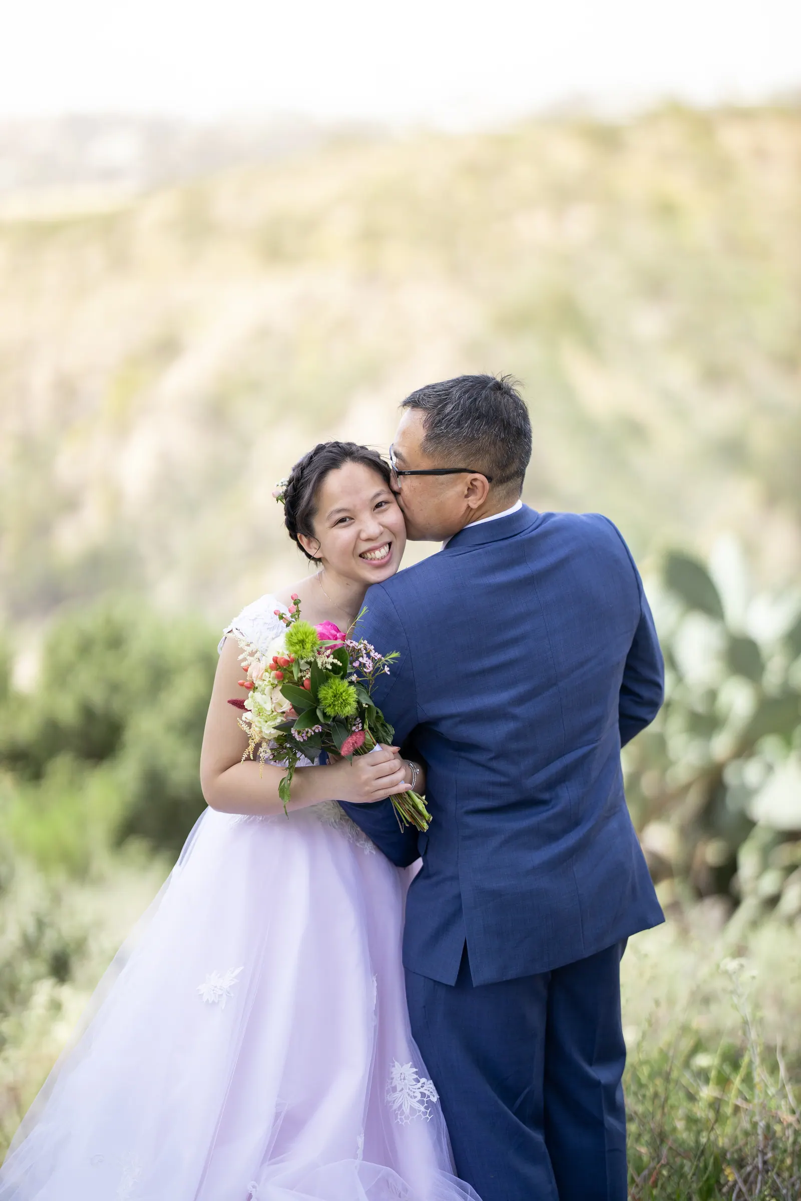 Groom kissing the bride on the cheek as she holds her bouquet