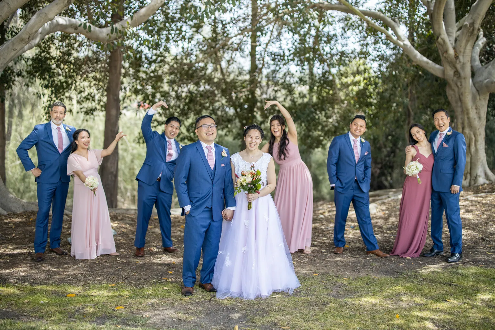 Wedding party posing playfully on the grass under trees