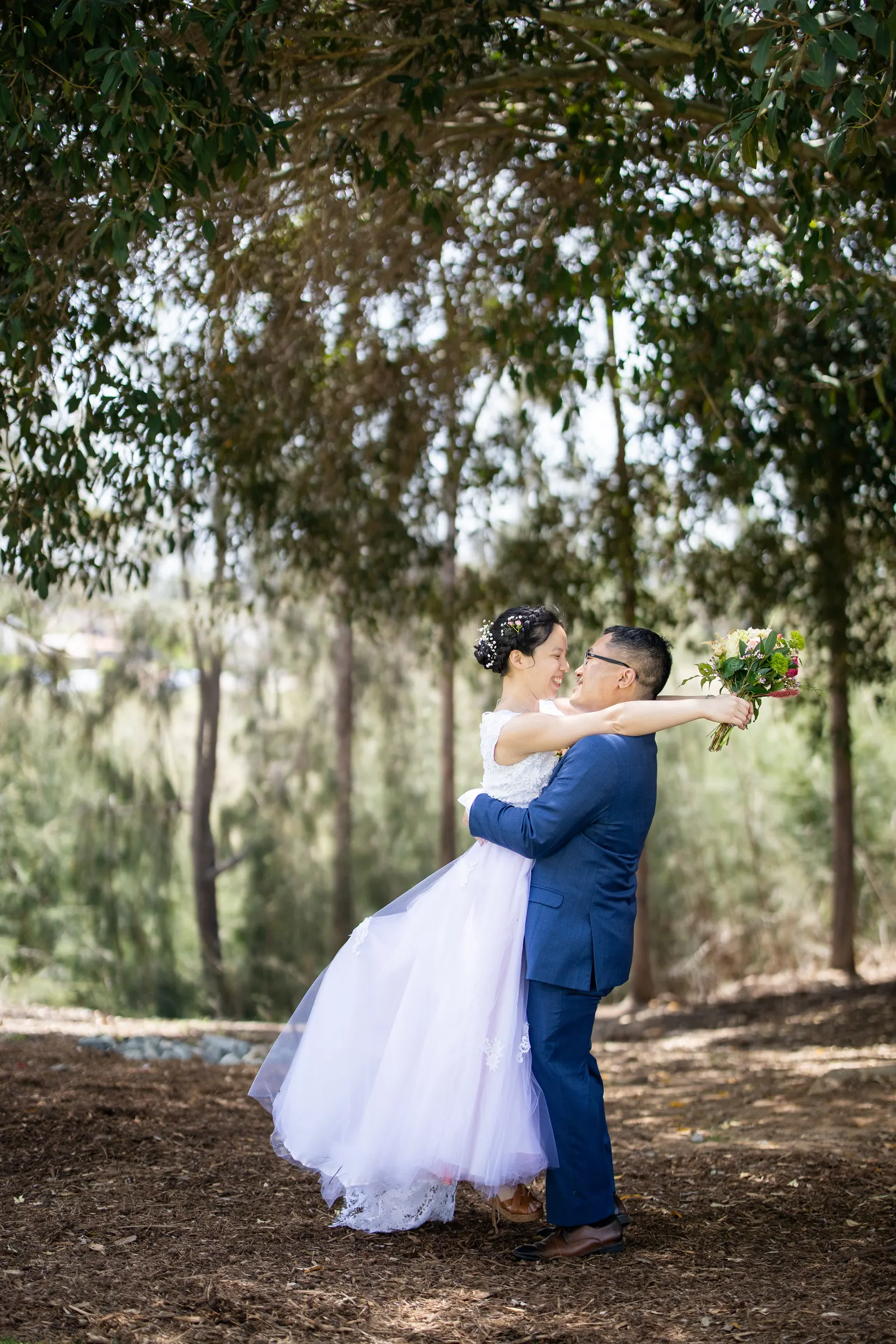 Groom lifting and kissing the bride among trees