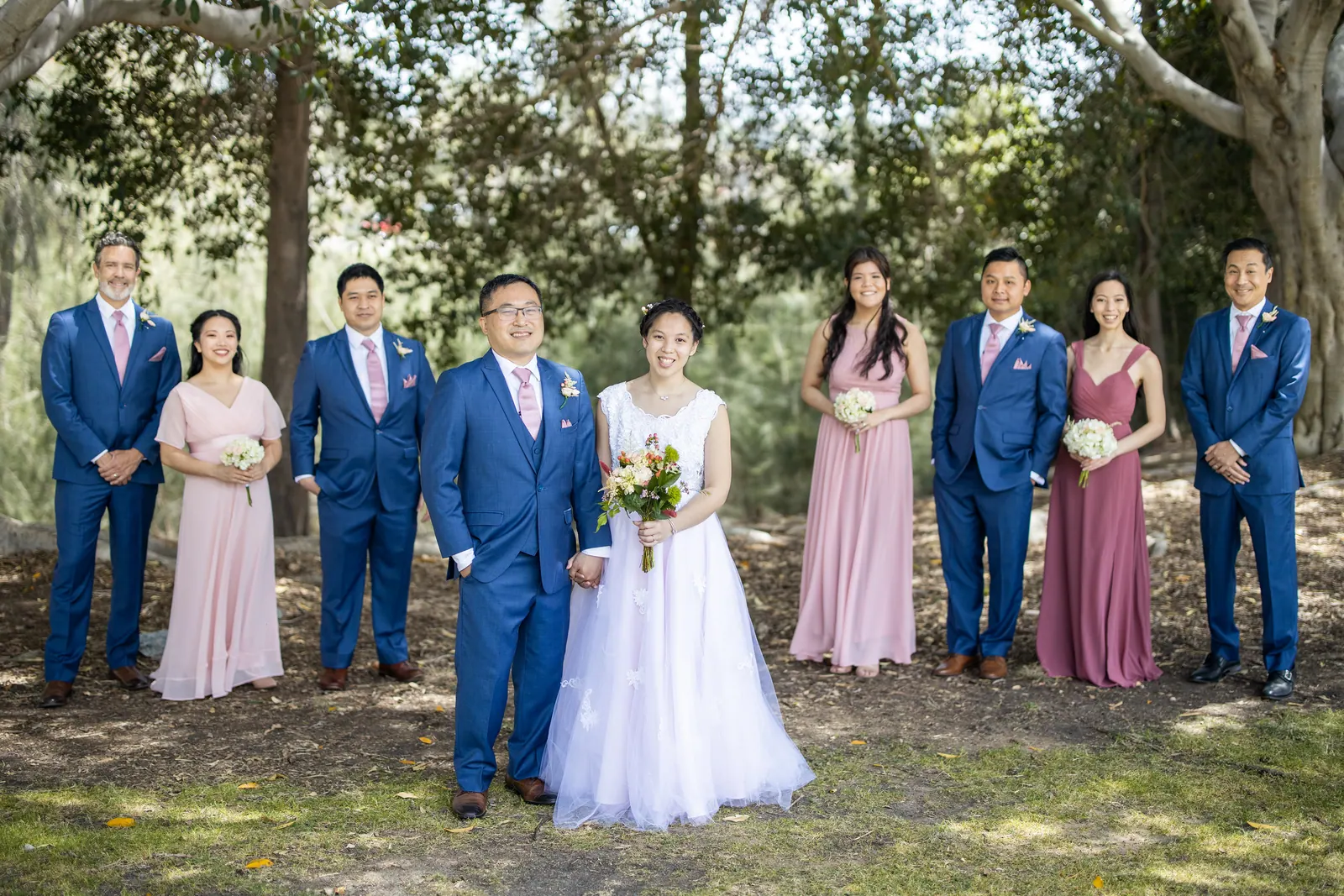 Full wedding party in navy and blush standing under trees