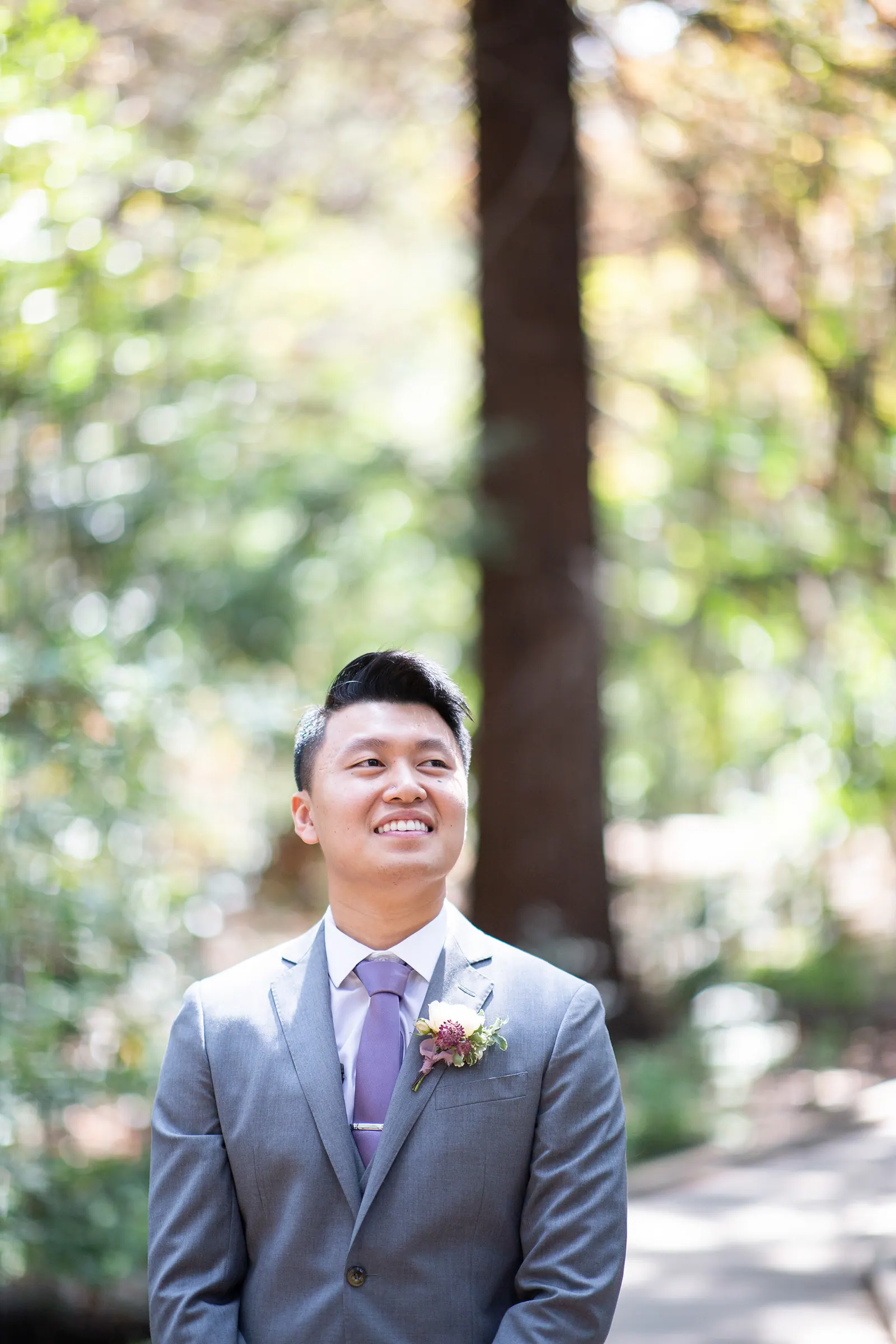 Groom in a grey suit smiling among redwood trees