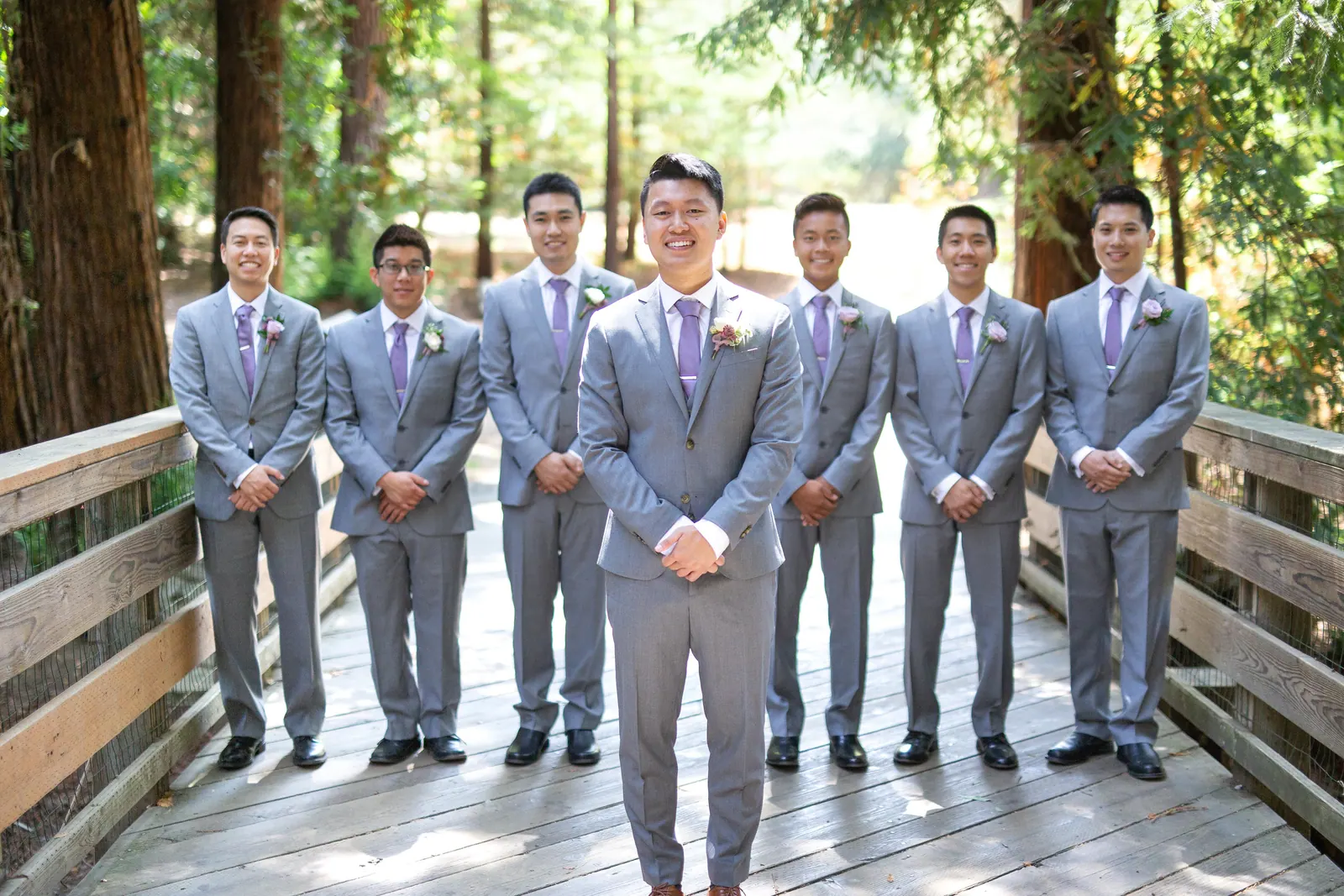 Groom and groomsmen in grey suits on a forest bridge