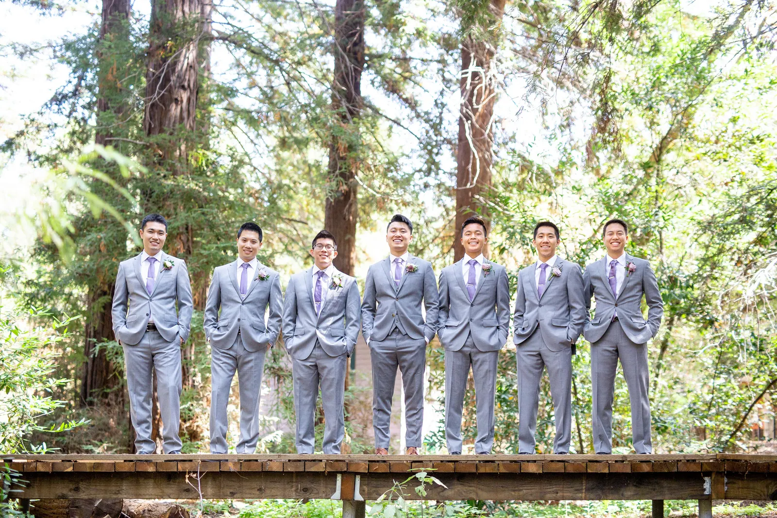 Groomsmen in grey suits lined up along a wooden railing