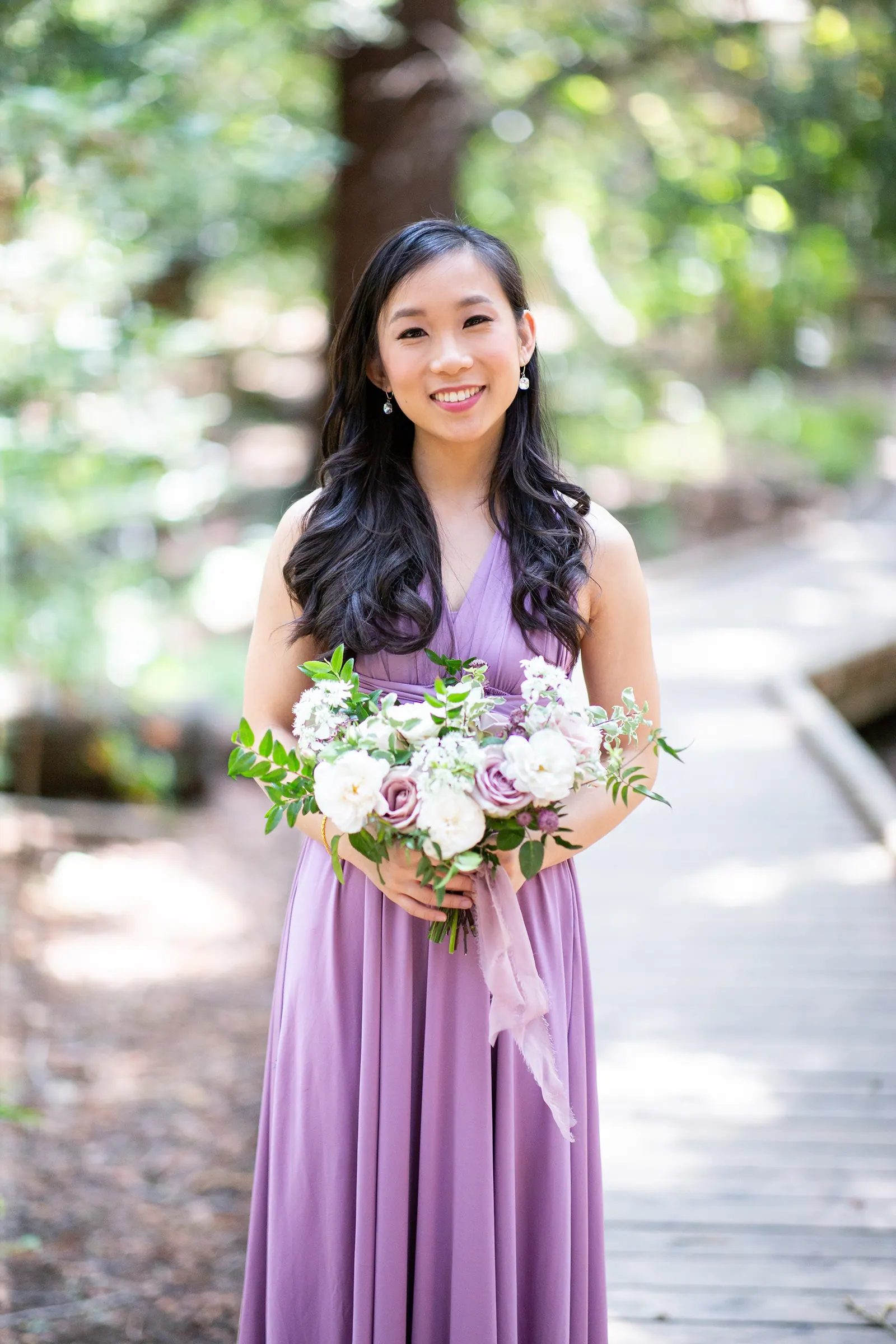 Bridesmaid in a lavender dress smiling on a forest path