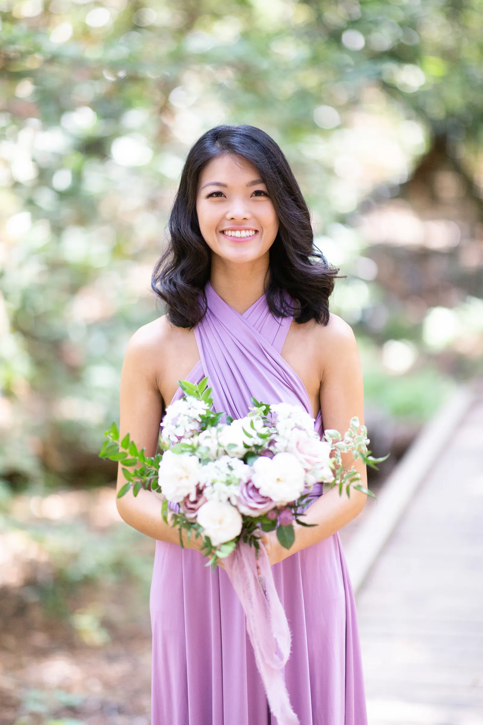 Bridesmaid in a lavender one-shoulder dress holding flowers
