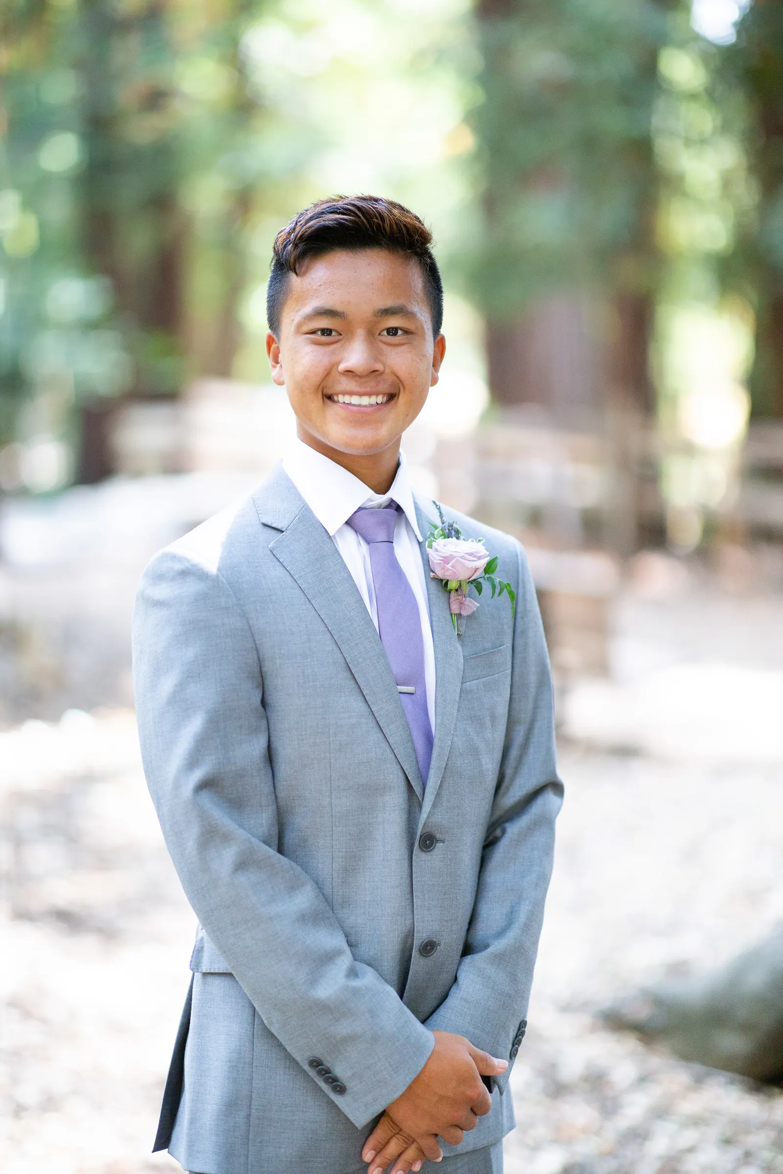 Smiling groomsman in a grey suit among trees